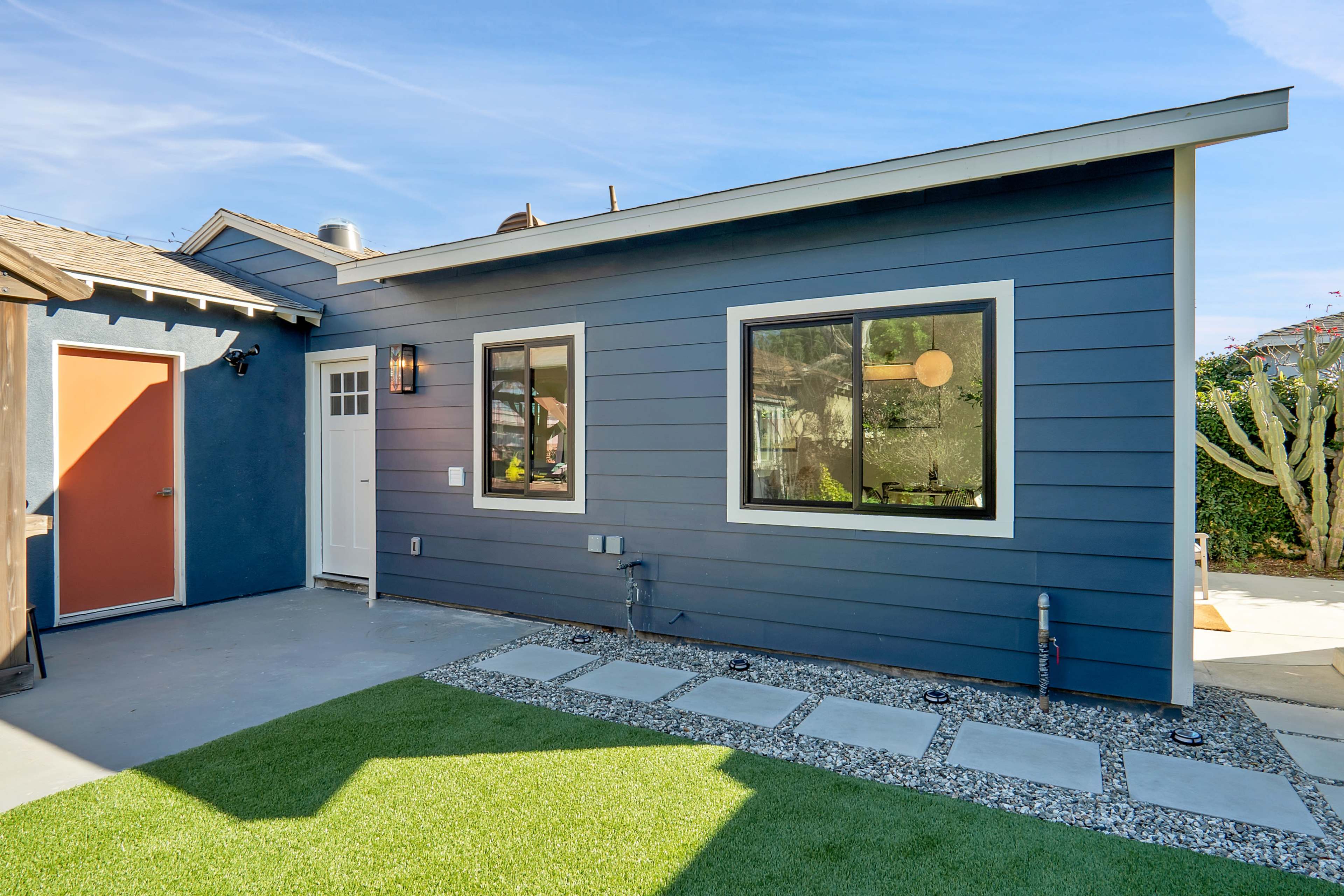 A modern blue house exterior with a light gray concrete area and stone pathways leading through a lawn.