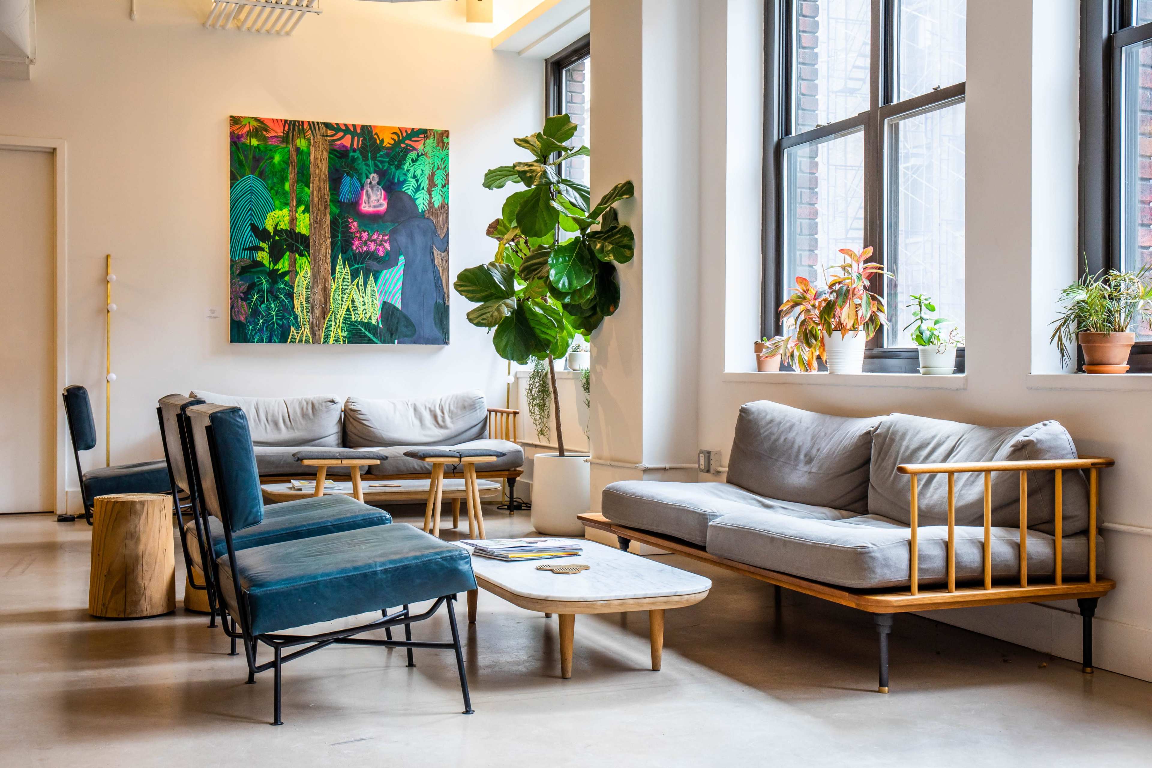 A modern lounge area with plush seating, a marble coffee table, and large windows, illuminated by natural light, alongside vibrant wall art.