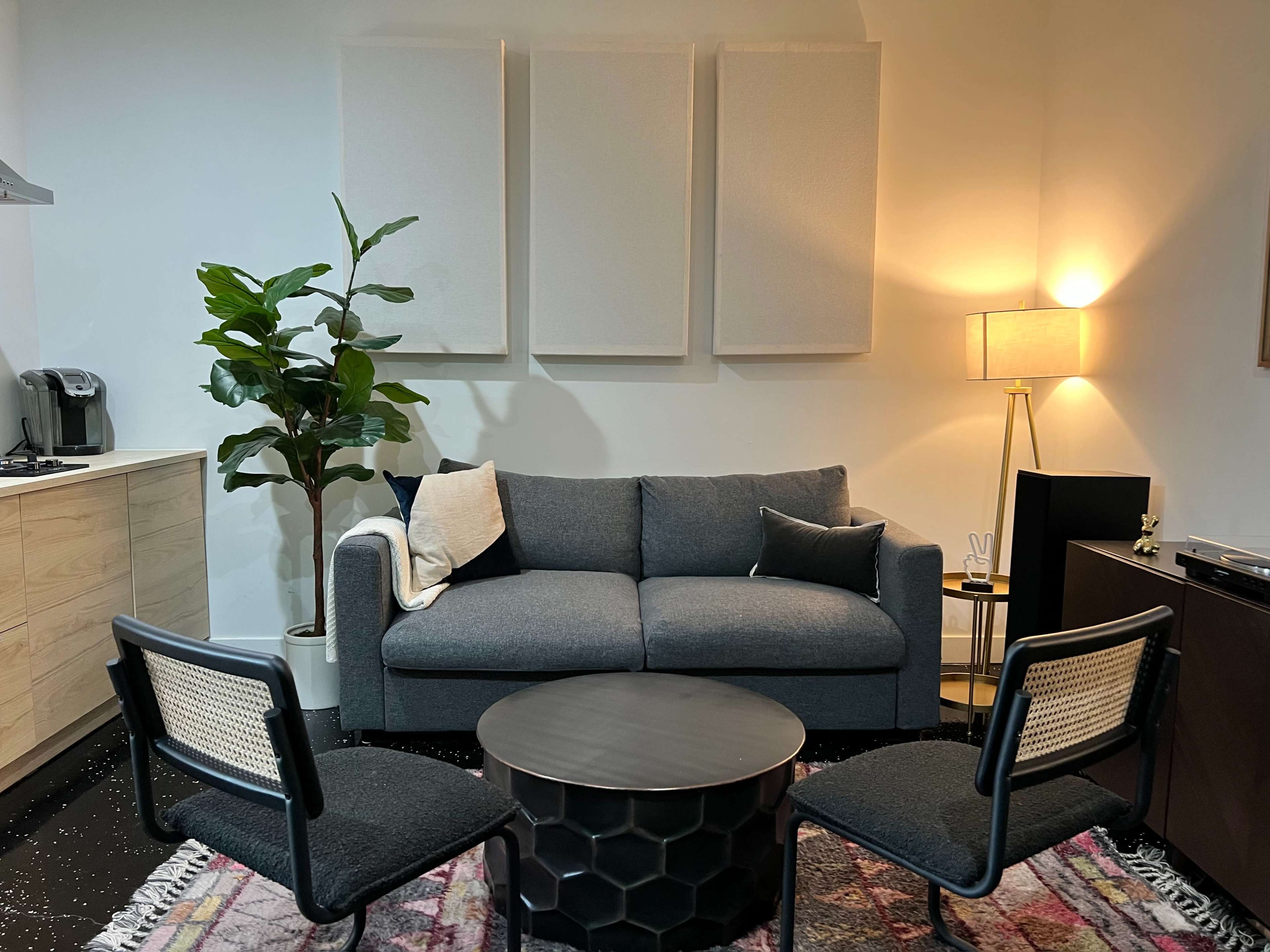 A modern living space featuring a gray sofa, two black accent chairs, a round coffee table, and a plant, with light-colored walls and a floor rug.