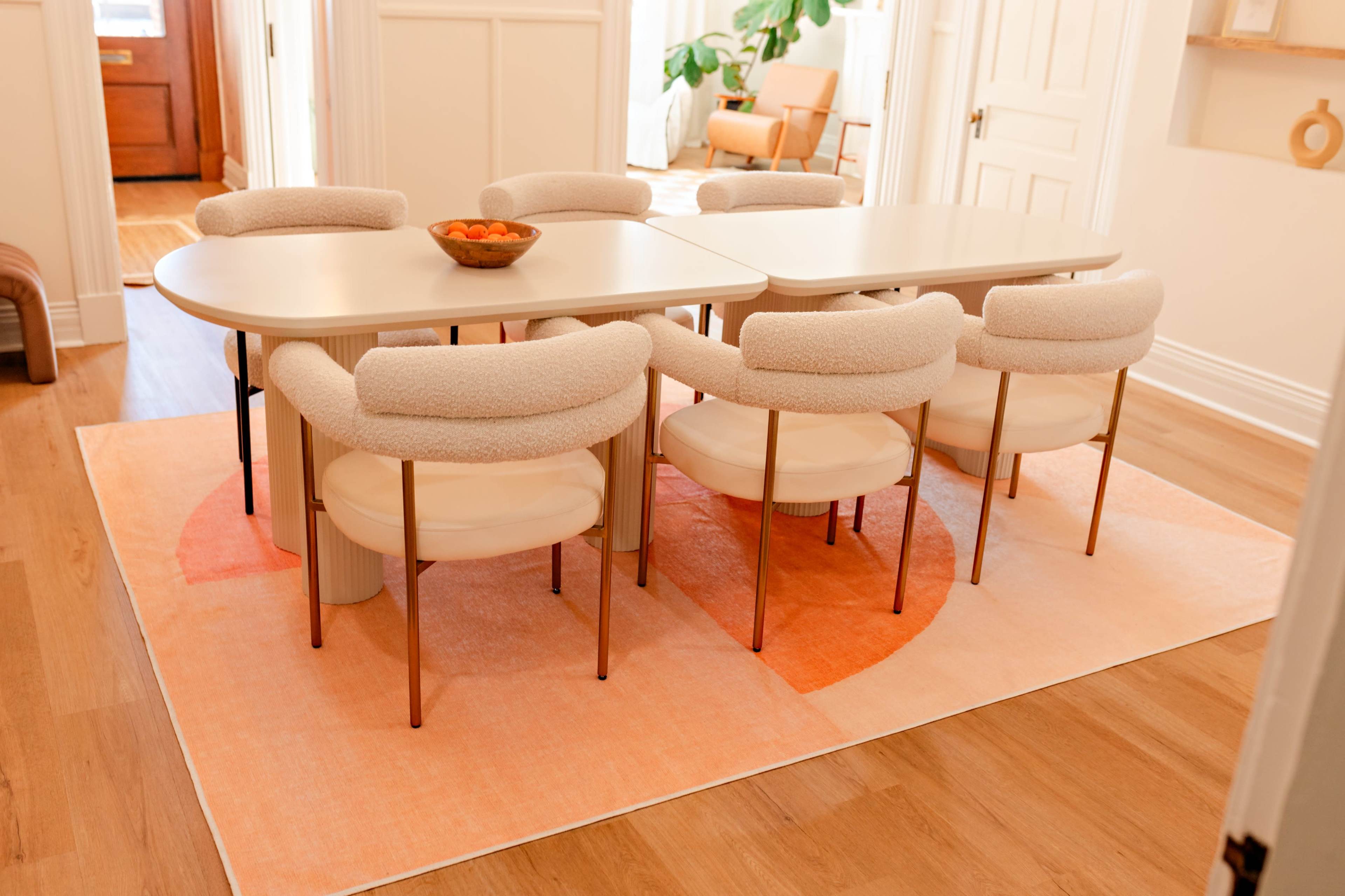 A modern dining table surrounded by upholstered chairs is set on a large, colorful area rug in a well-lit room.