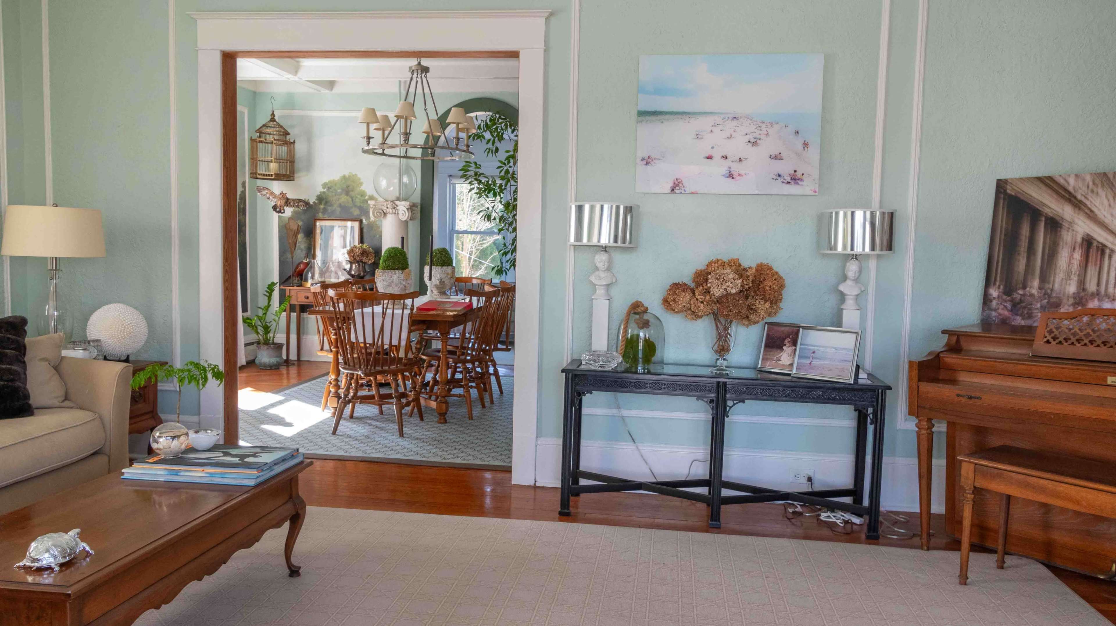 The image shows a居 living room with a piano, a coffee table, and a view into a dining area featuring wooden furniture and decor.
