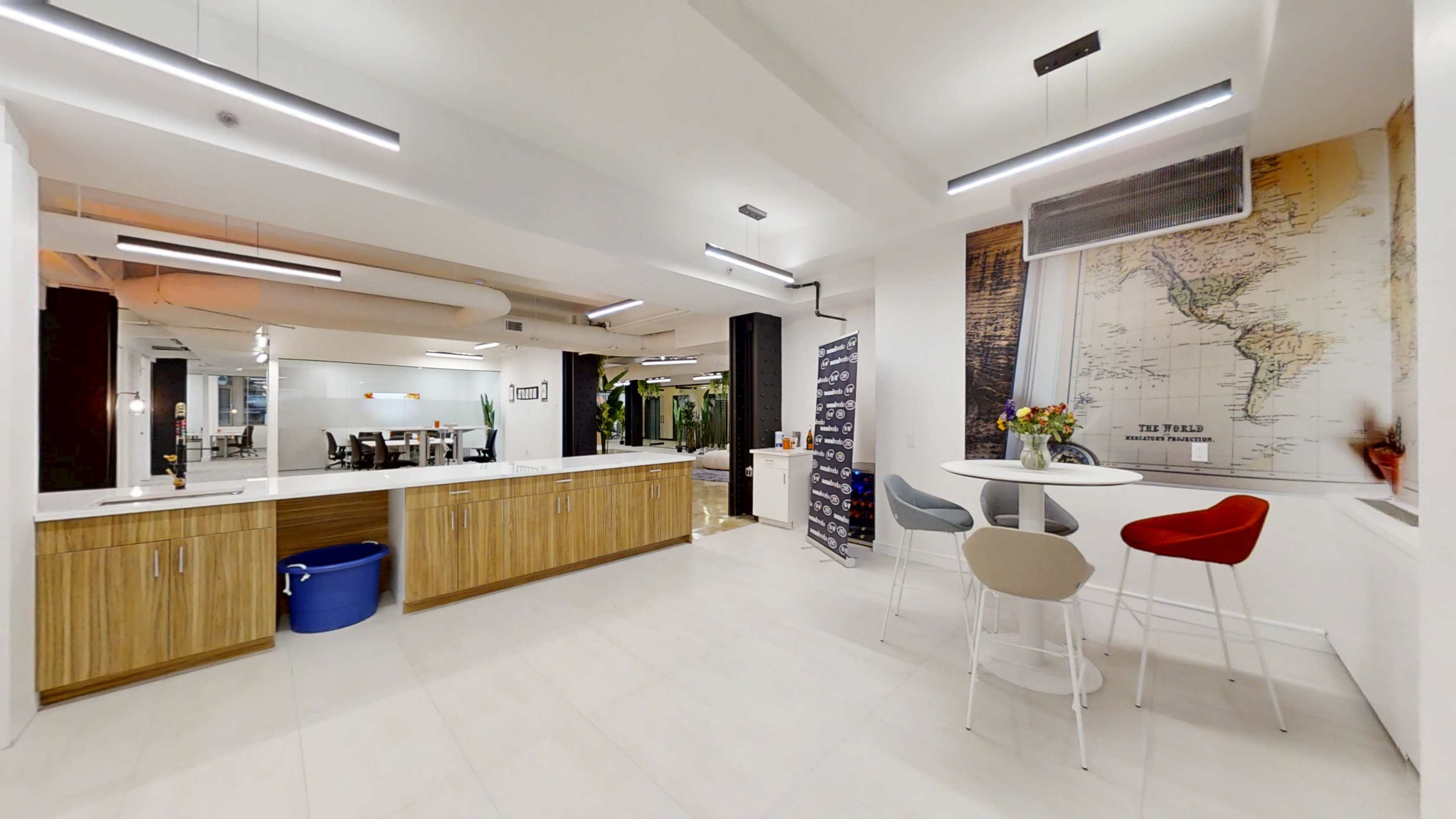 The image shows a modern kitchen area with wooden cabinets, a white countertop, and a seating arrangement featuring three chairs and a small table.