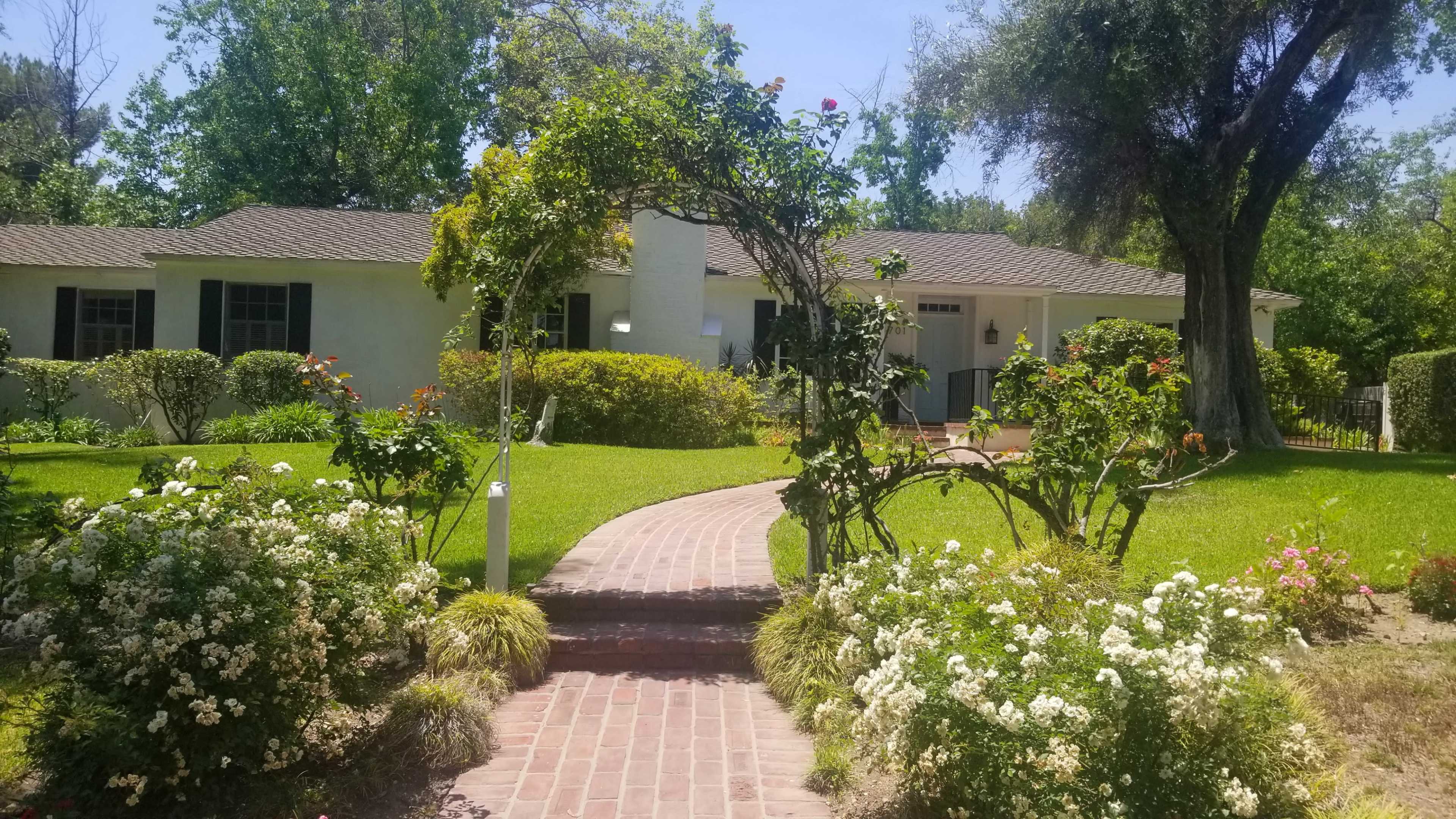 A brick pathway leads to a house surrounded by well-maintained gardens and greenery.