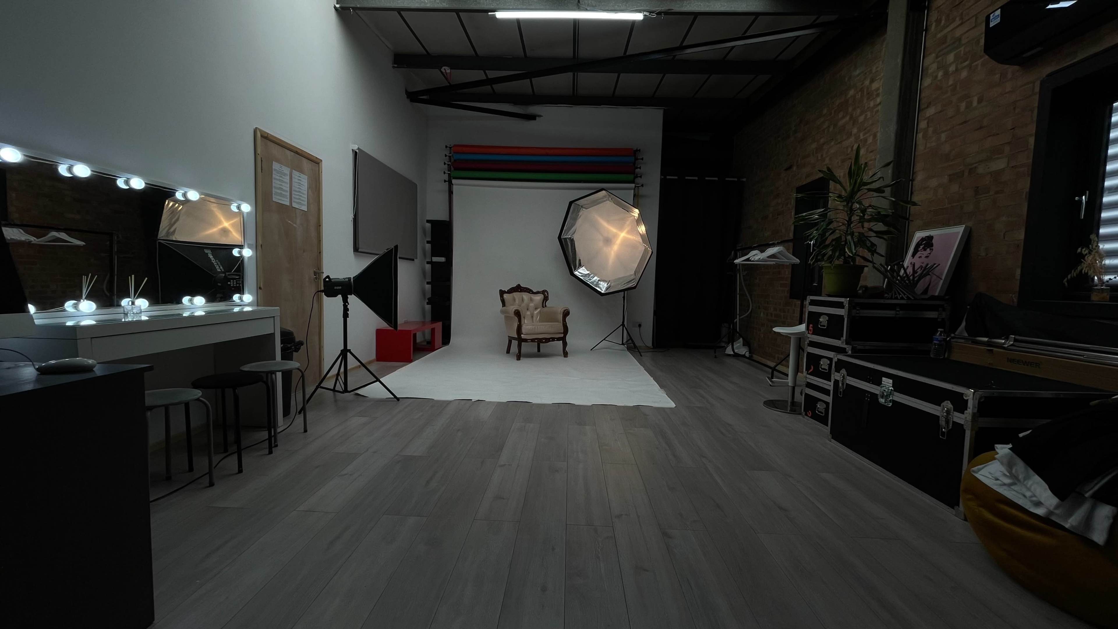 A spacious photography studio featuring a central chair on a white backdrop, with various lighting equipment and mirrors along the walls.