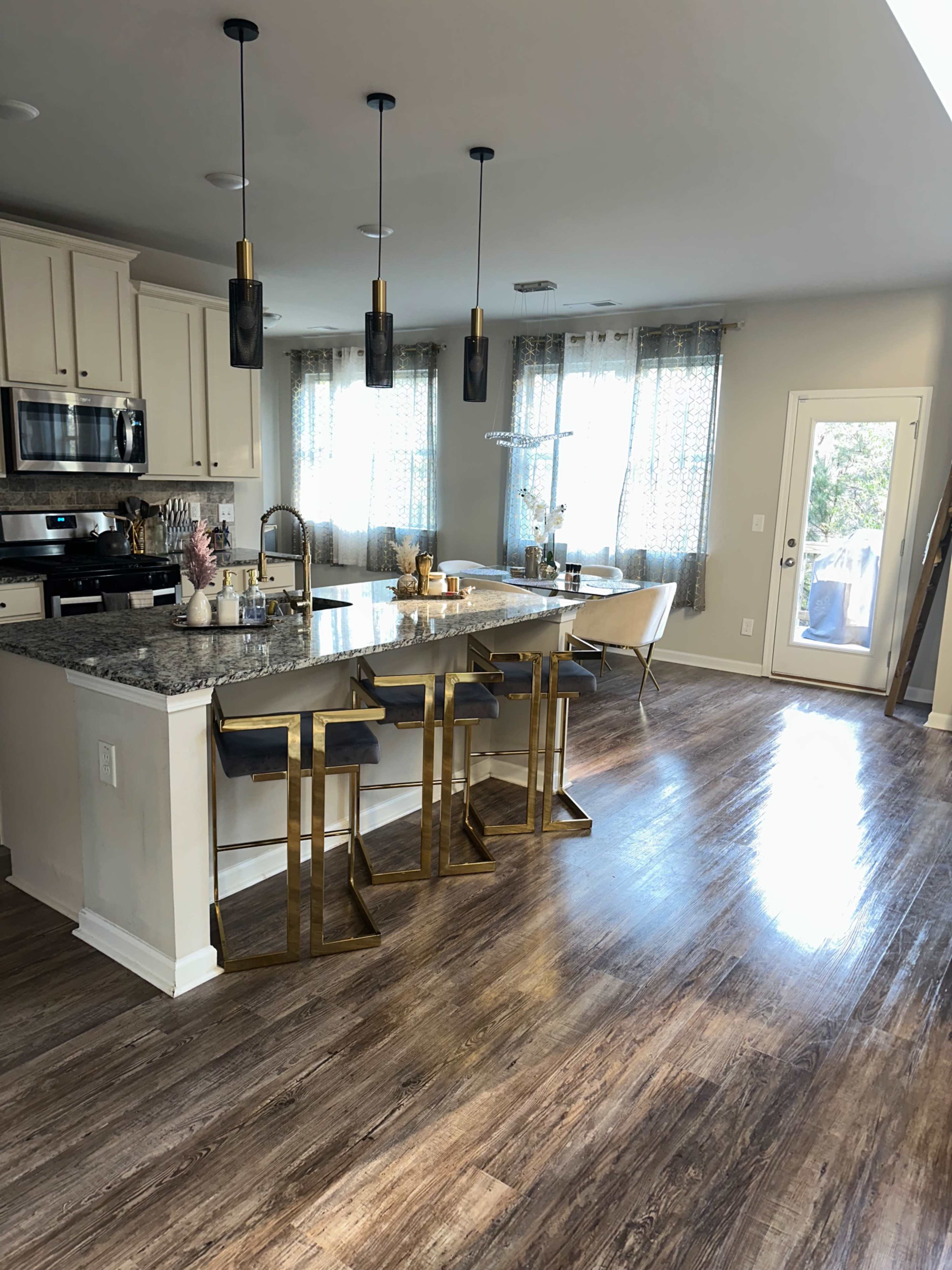 A modern kitchen with a granite island, four high stools, and large windows allowing natural light.