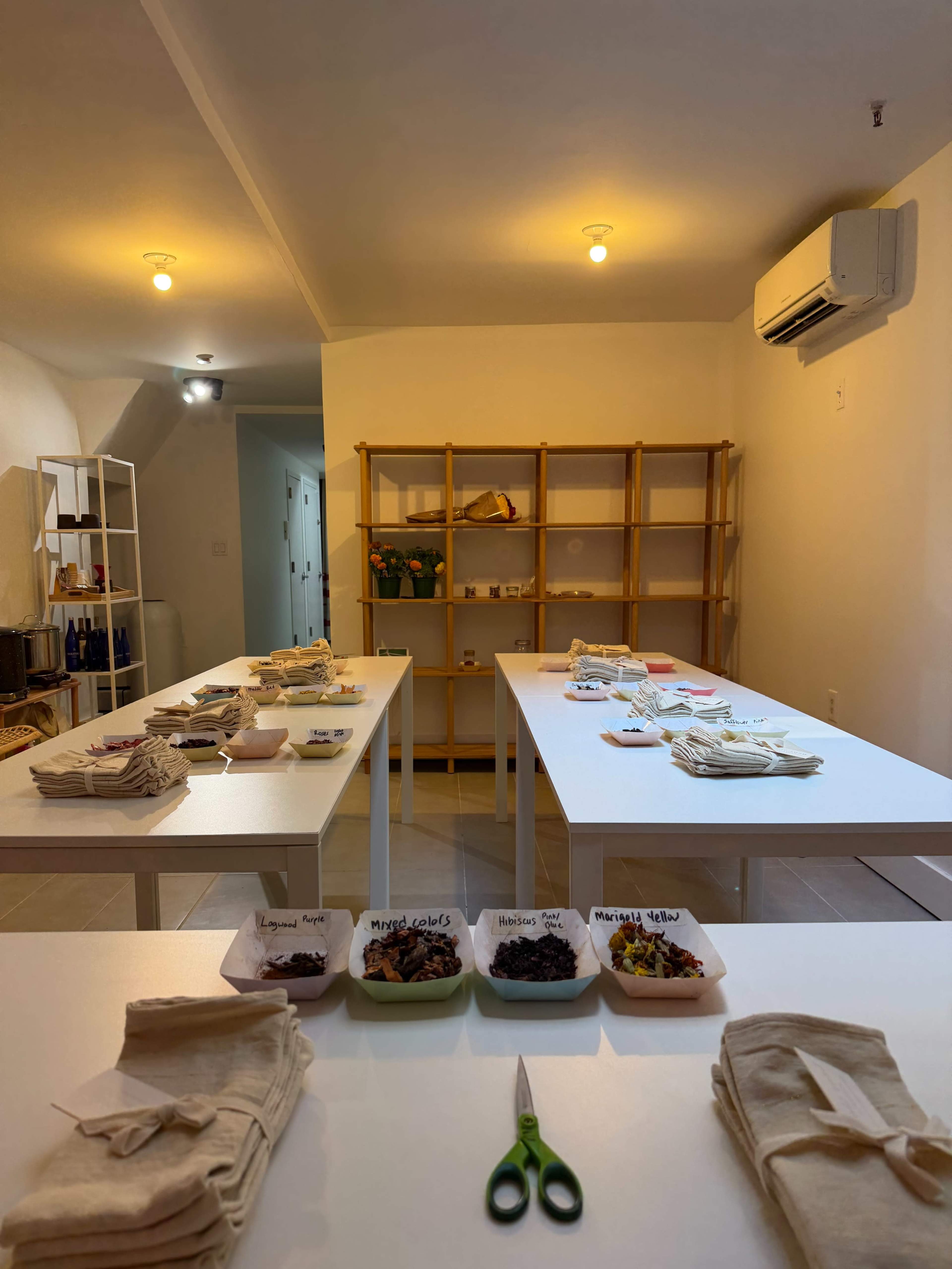 The image shows a bright, tidy room with several white tables arranged in rows, each displaying neatly organized containers of food items and utensils.