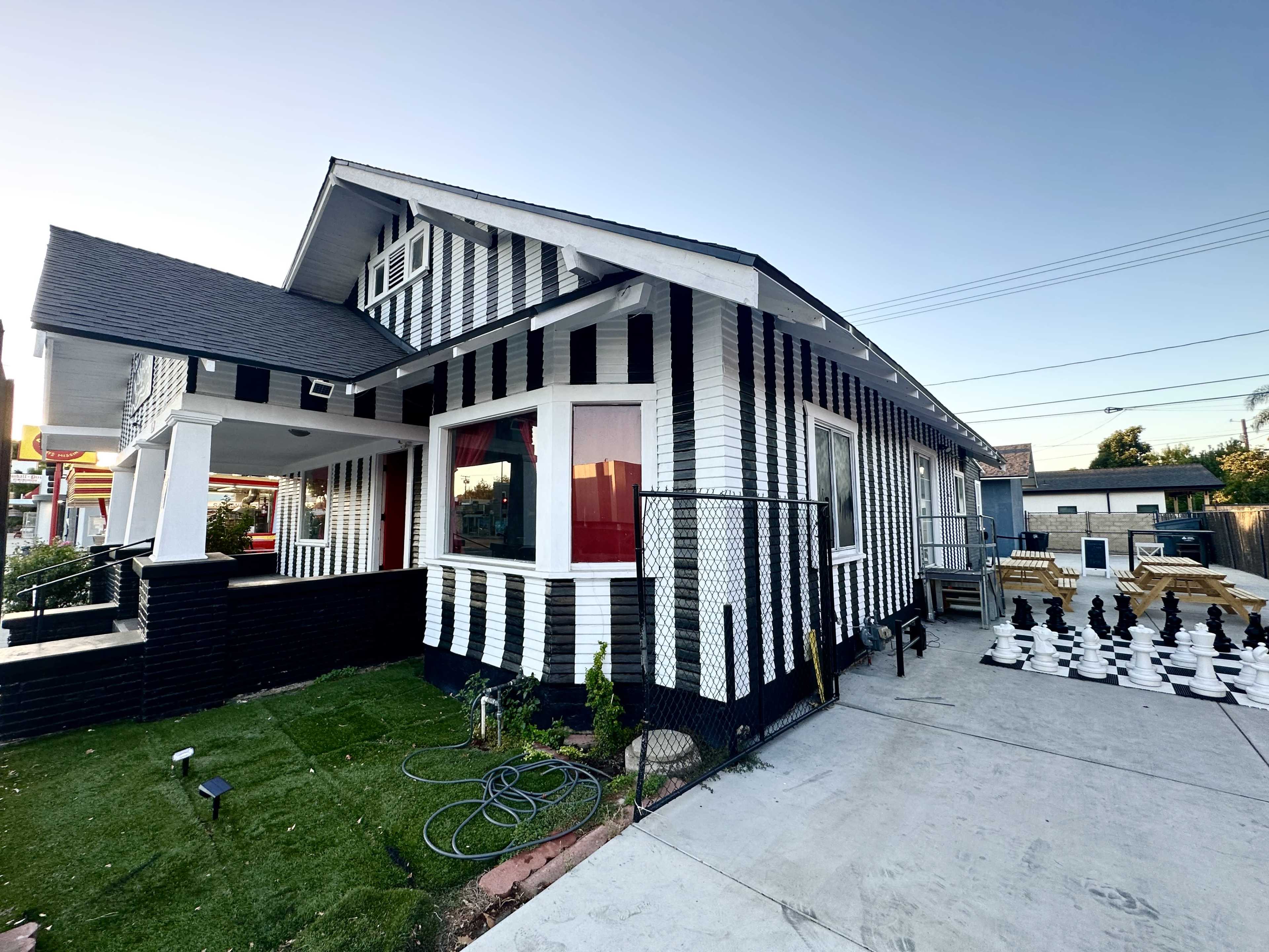 A house with a distinctive black and white striped exterior, featuring a front yard with a neatly maintained lawn and large outdoor chess pieces.