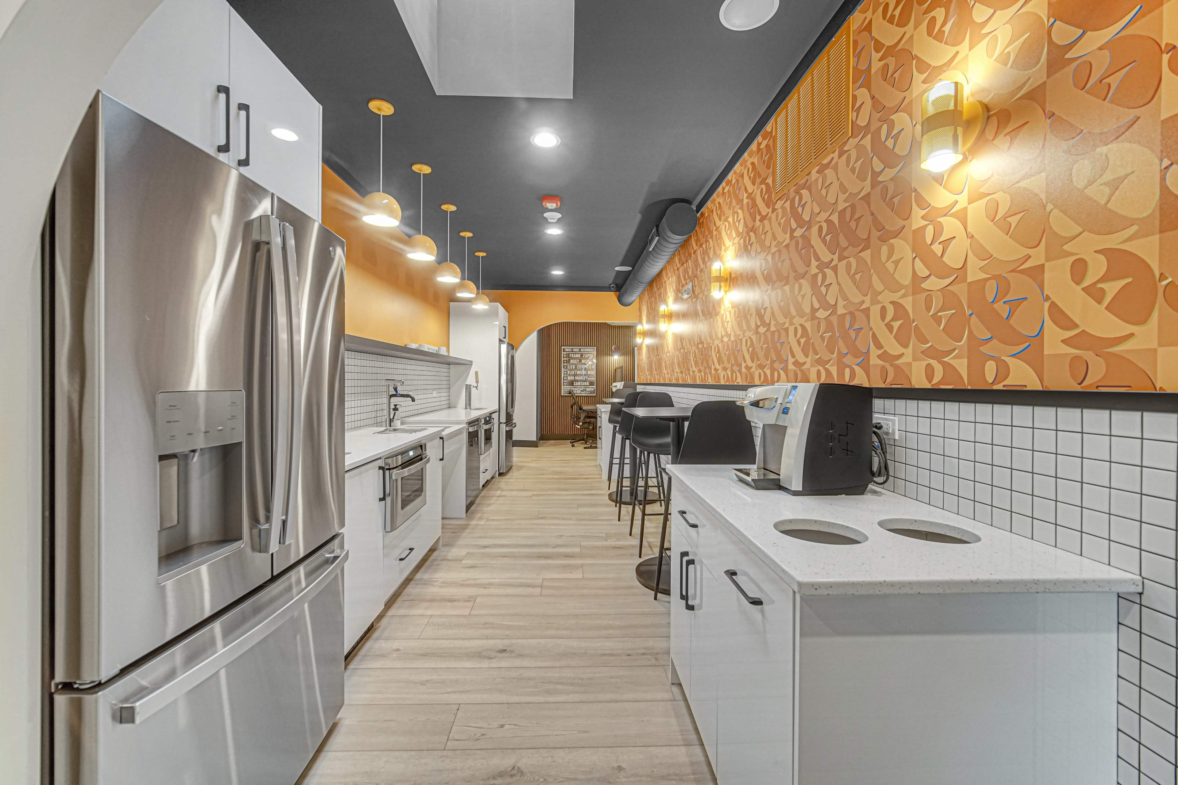 The image shows a modern kitchen with stainless steel appliances, white cabinetry, and orange patterned wallpaper.