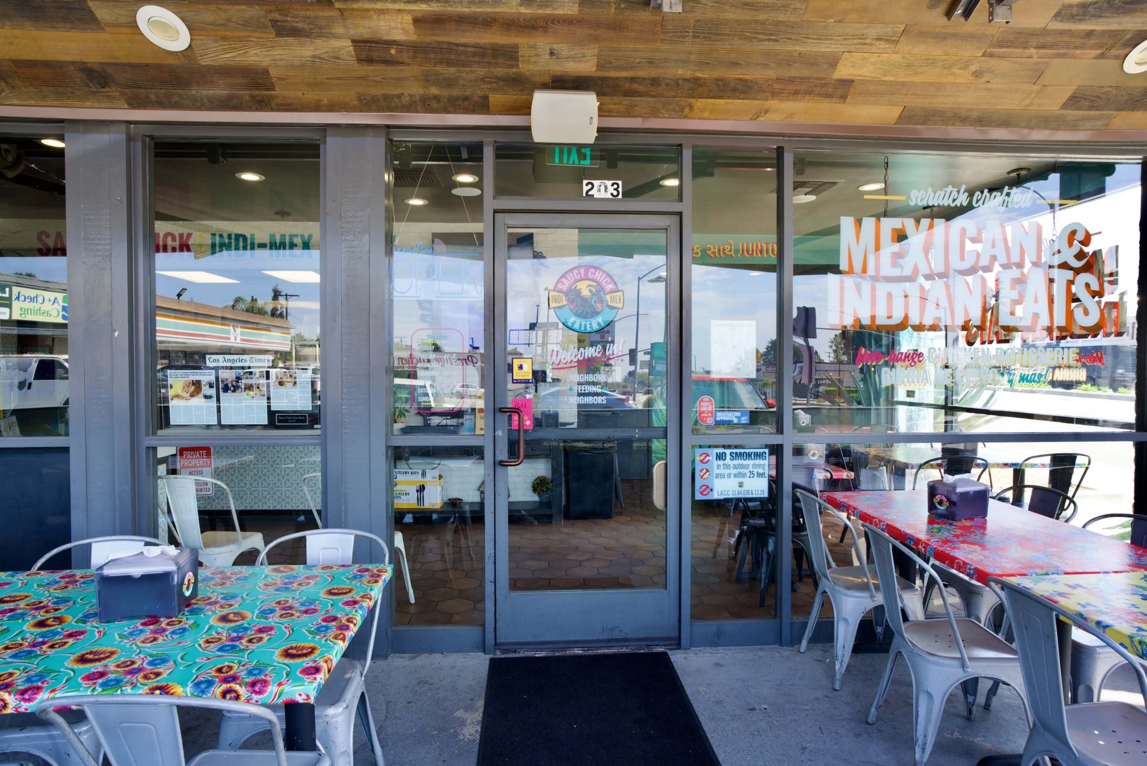 The image shows the entrance of a restaurant featuring brightly colored tables and signage indicating it serves Mexican and Indian food.