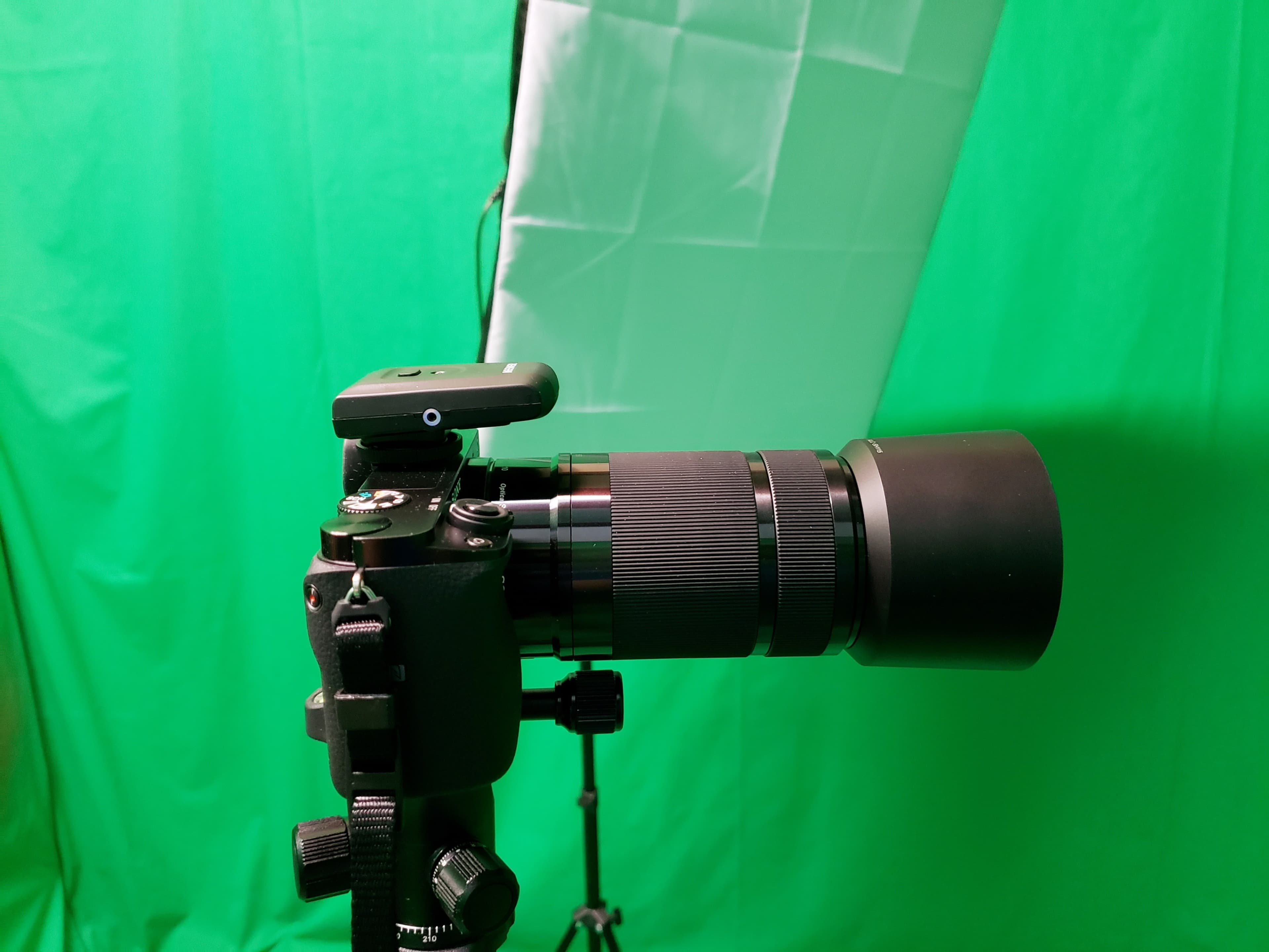 A camera with a large lens is mounted on a tripod in front of a green backdrop.