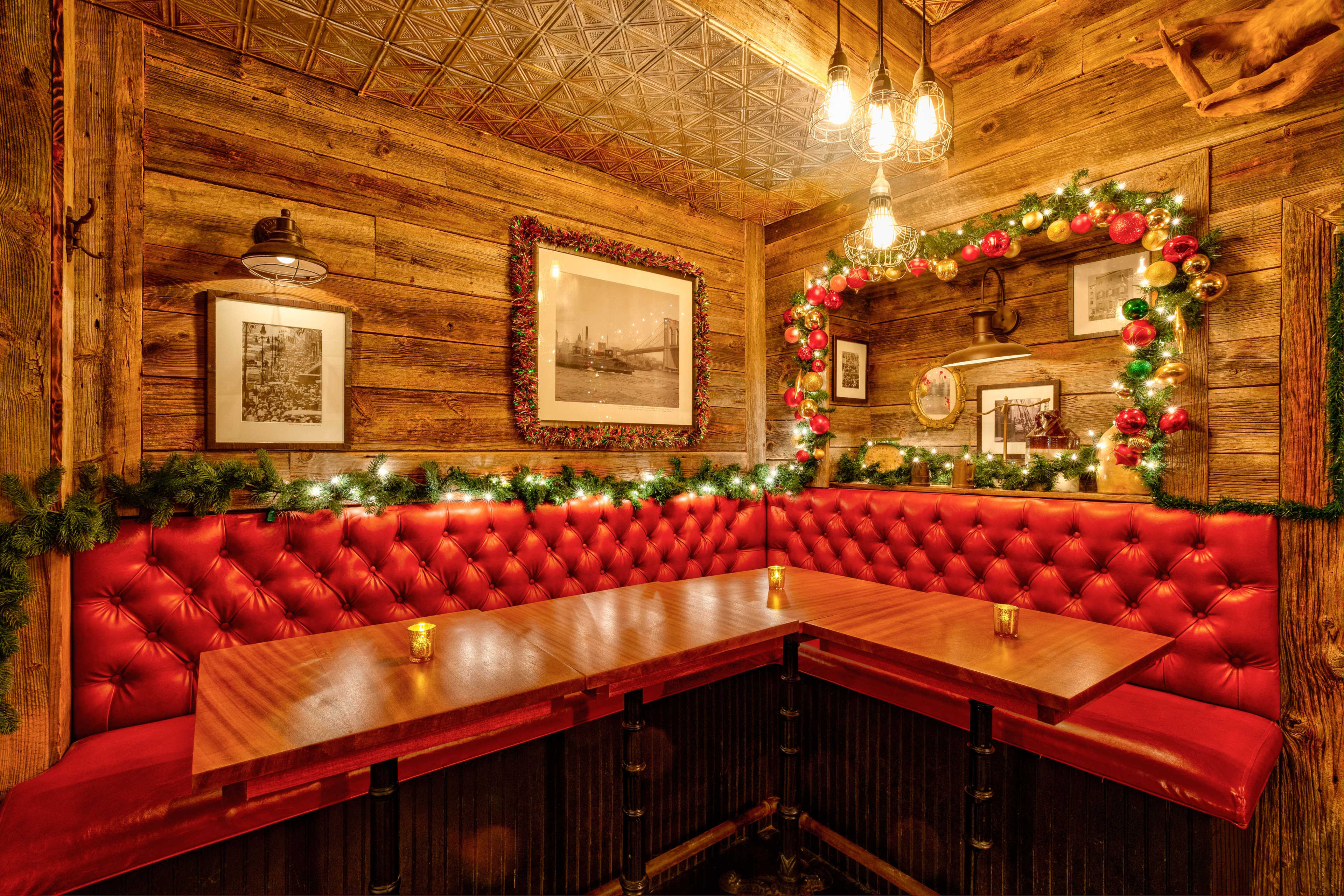 The image depicts a cozy restaurant corner with red tufted seating, wooden walls, and Christmas decorations of garlands and ornaments.