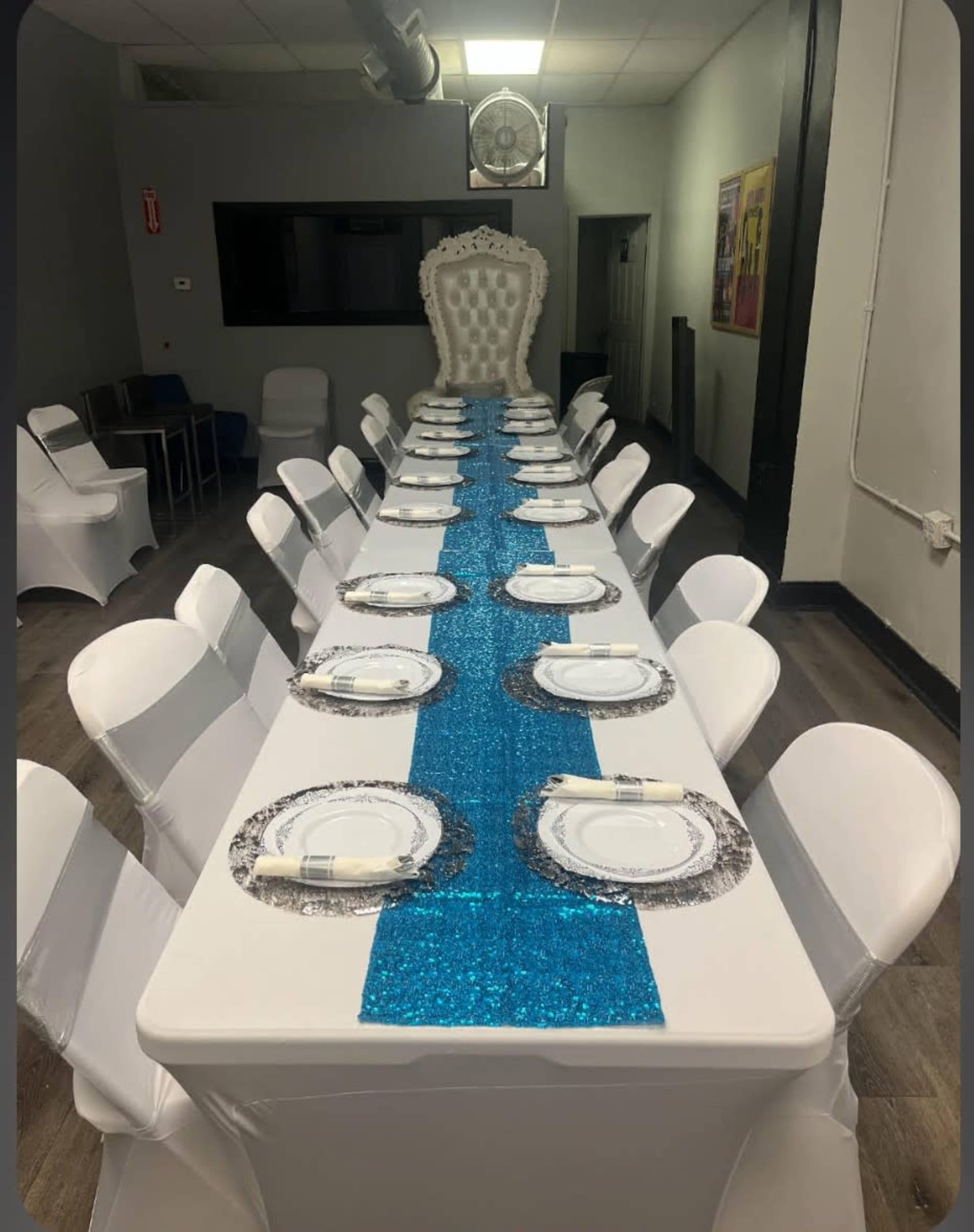A long banquet table is set with white chairs and blue glitter table runners, leading to a large ornate throne at one end.