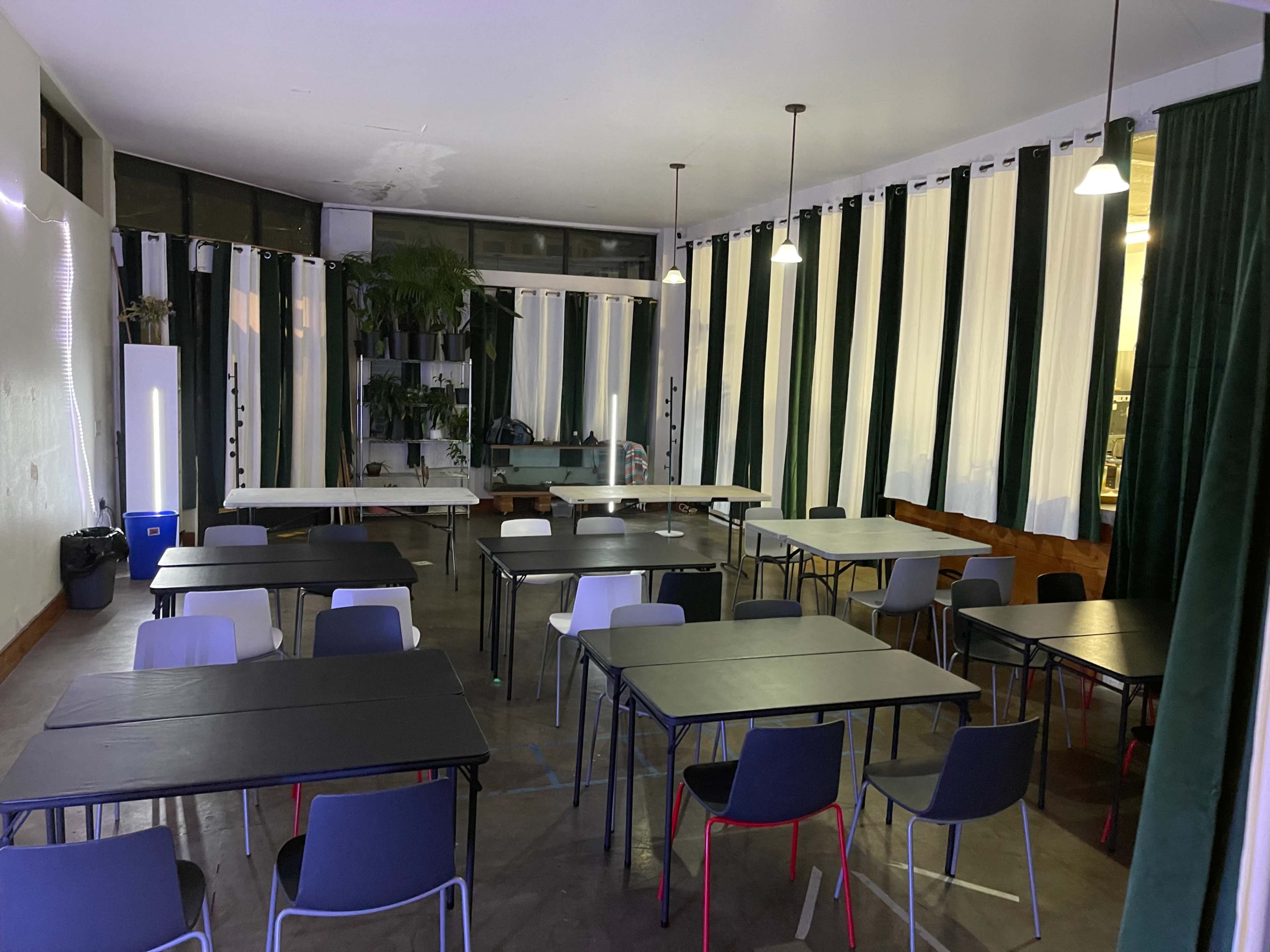 A spacious room with several tables and chairs arranged for a meeting, surrounded by large windows and curtains.
