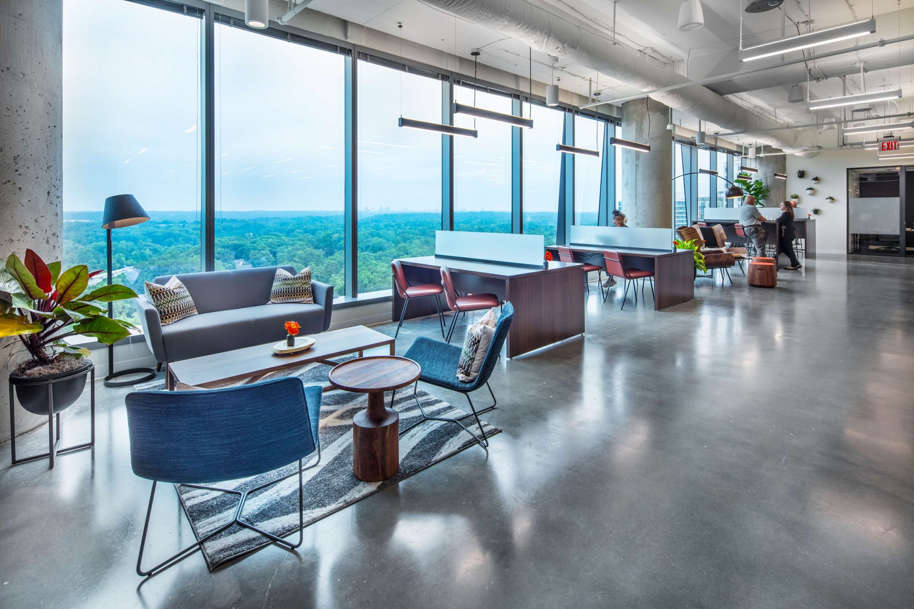 A modern office space with large windows offering a view of a city skyline, featuring various seating areas and plants.