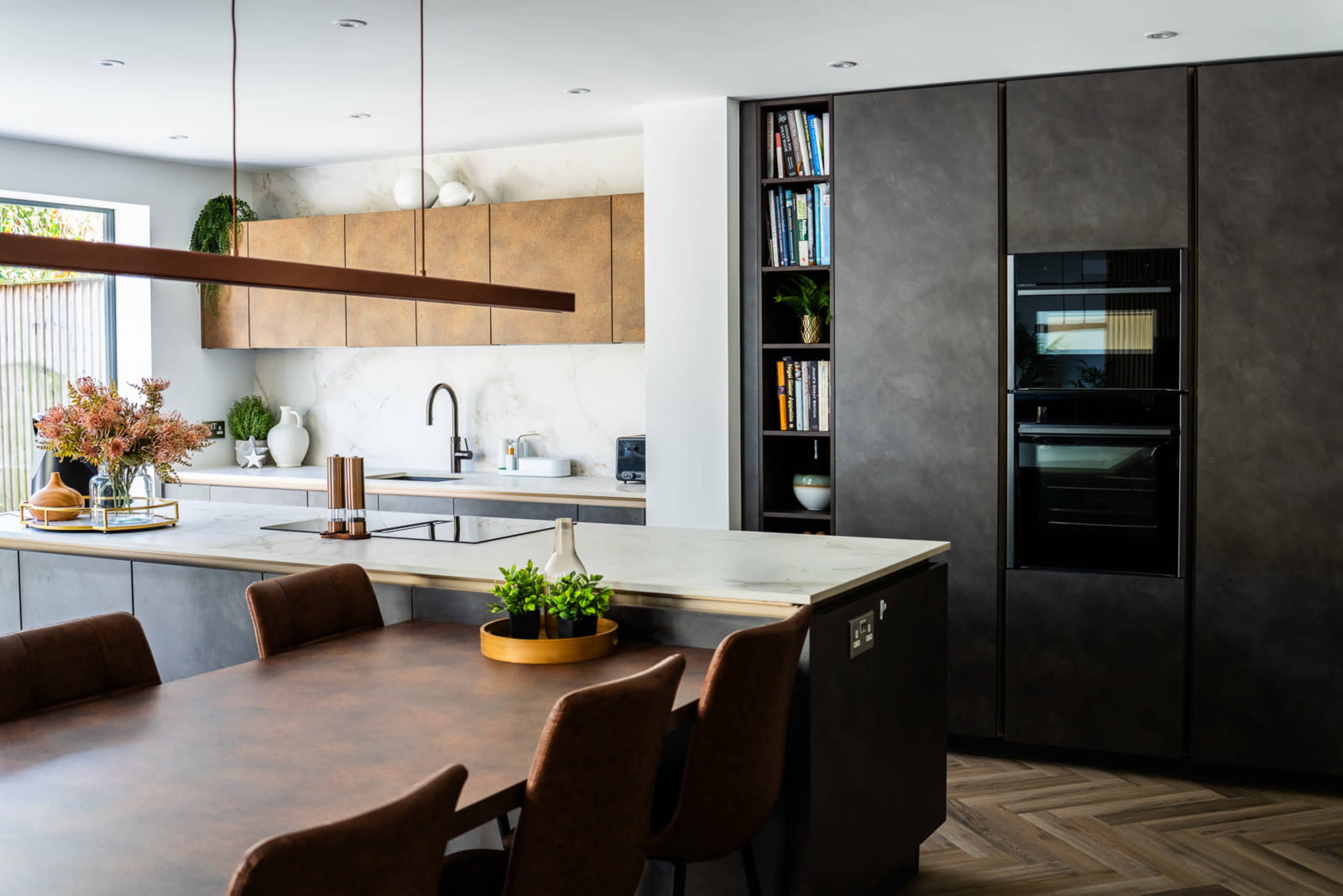 The image shows a modern kitchen featuring a central island, dark cabinetry, and a combination of stone and metal finishes.