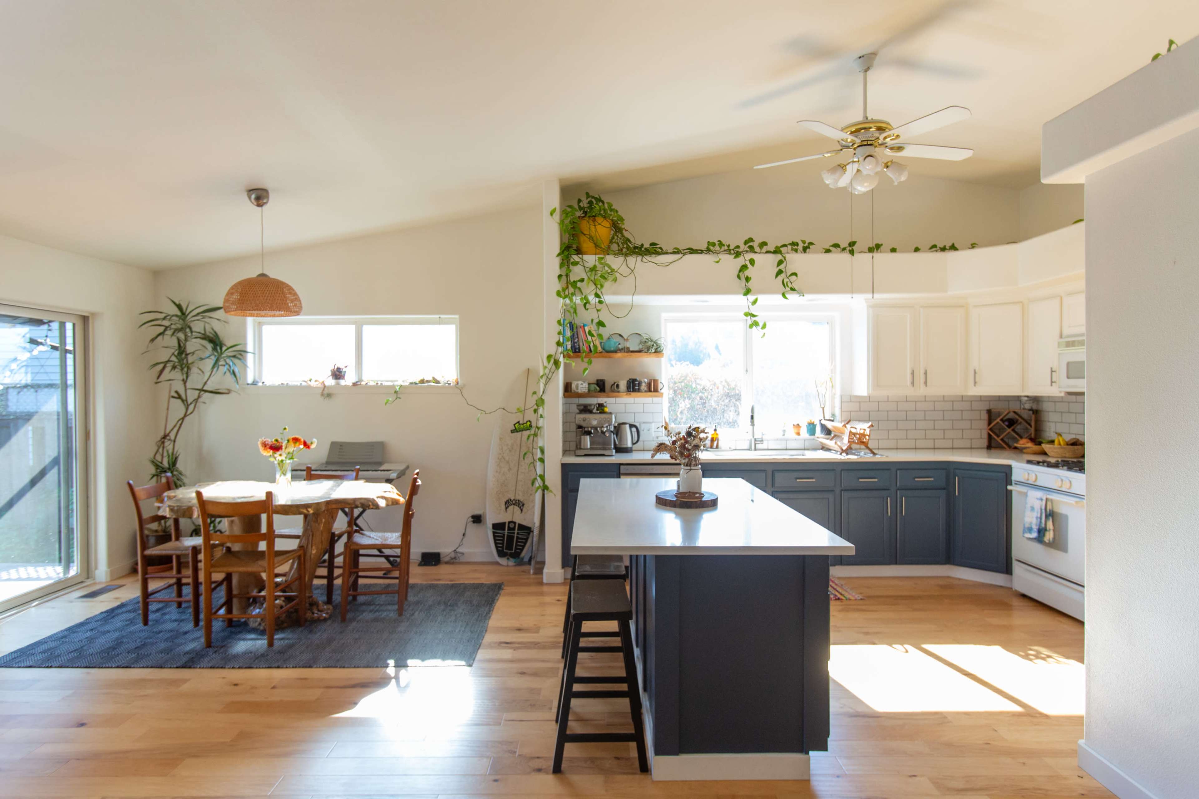 A bright kitchen features a central island, white cabinetry, and a dining area with wooden chairs and a table near a large window.