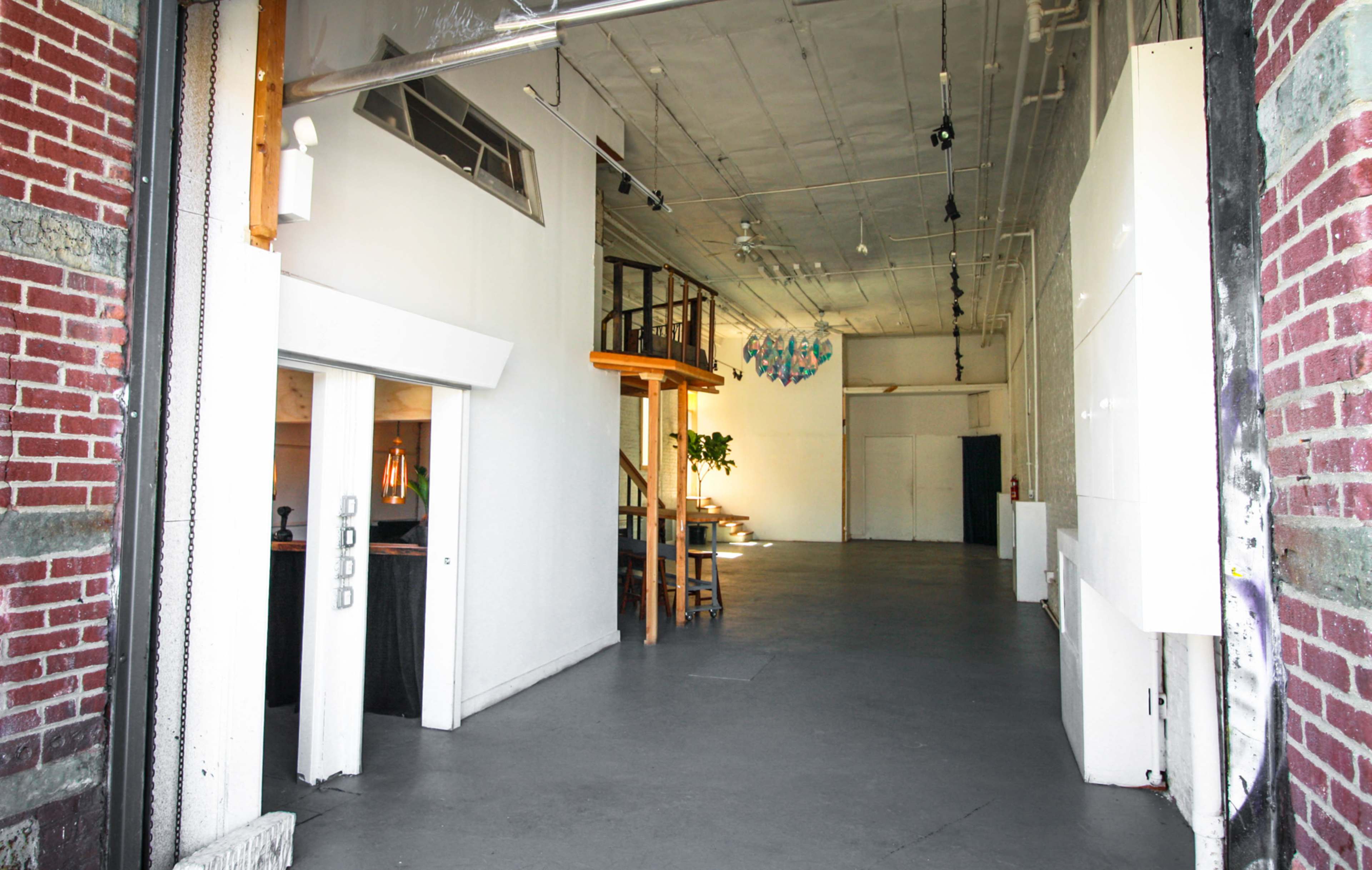 The image shows an open, industrial-style space with exposed ceilings, polished concrete floors, and a staircase leading to an upper area.