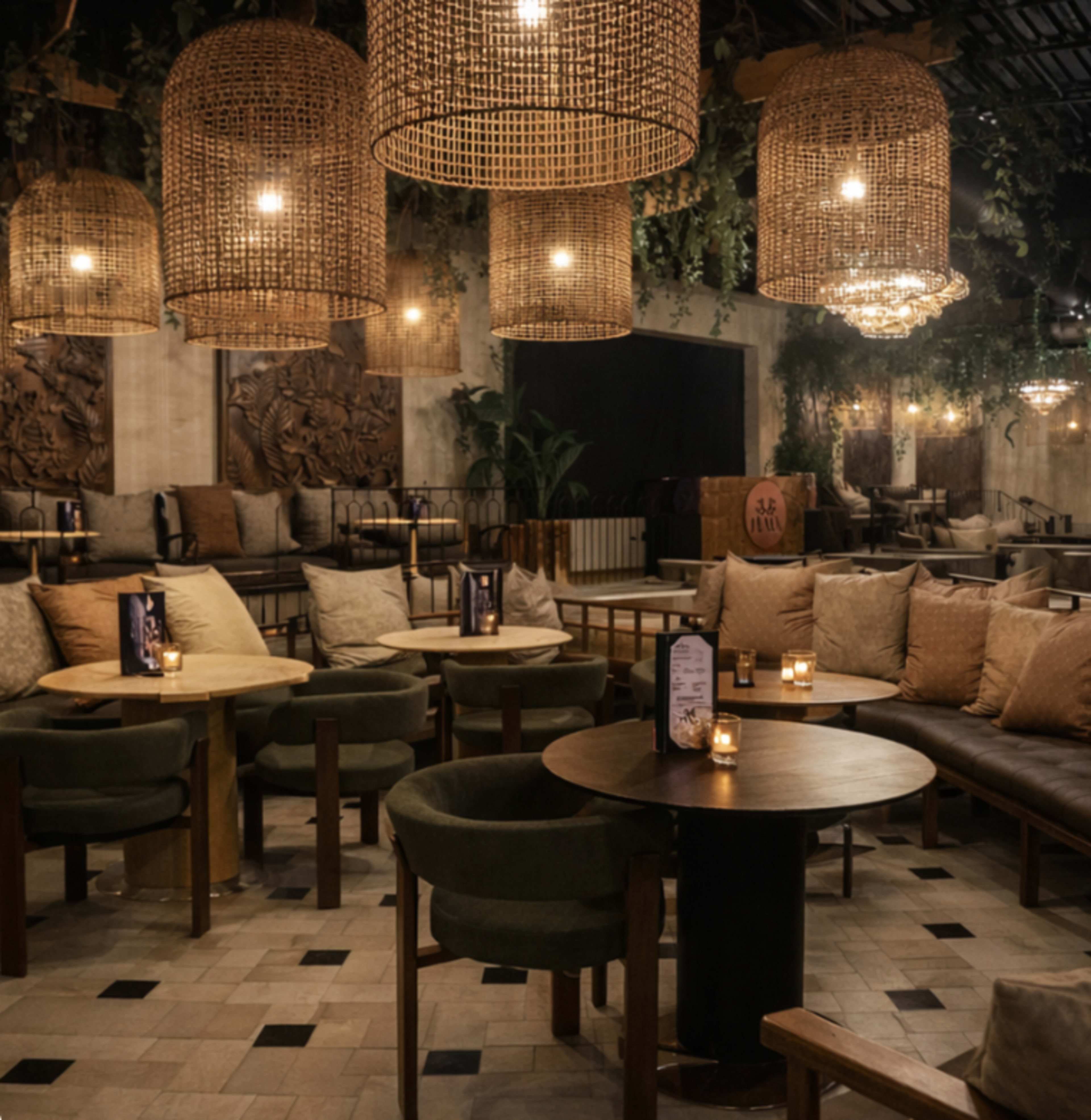 The image shows a cozy restaurant interior with woven pendant lights, plants, and a mix of seating arrangements including circular tables and cushioned benches.