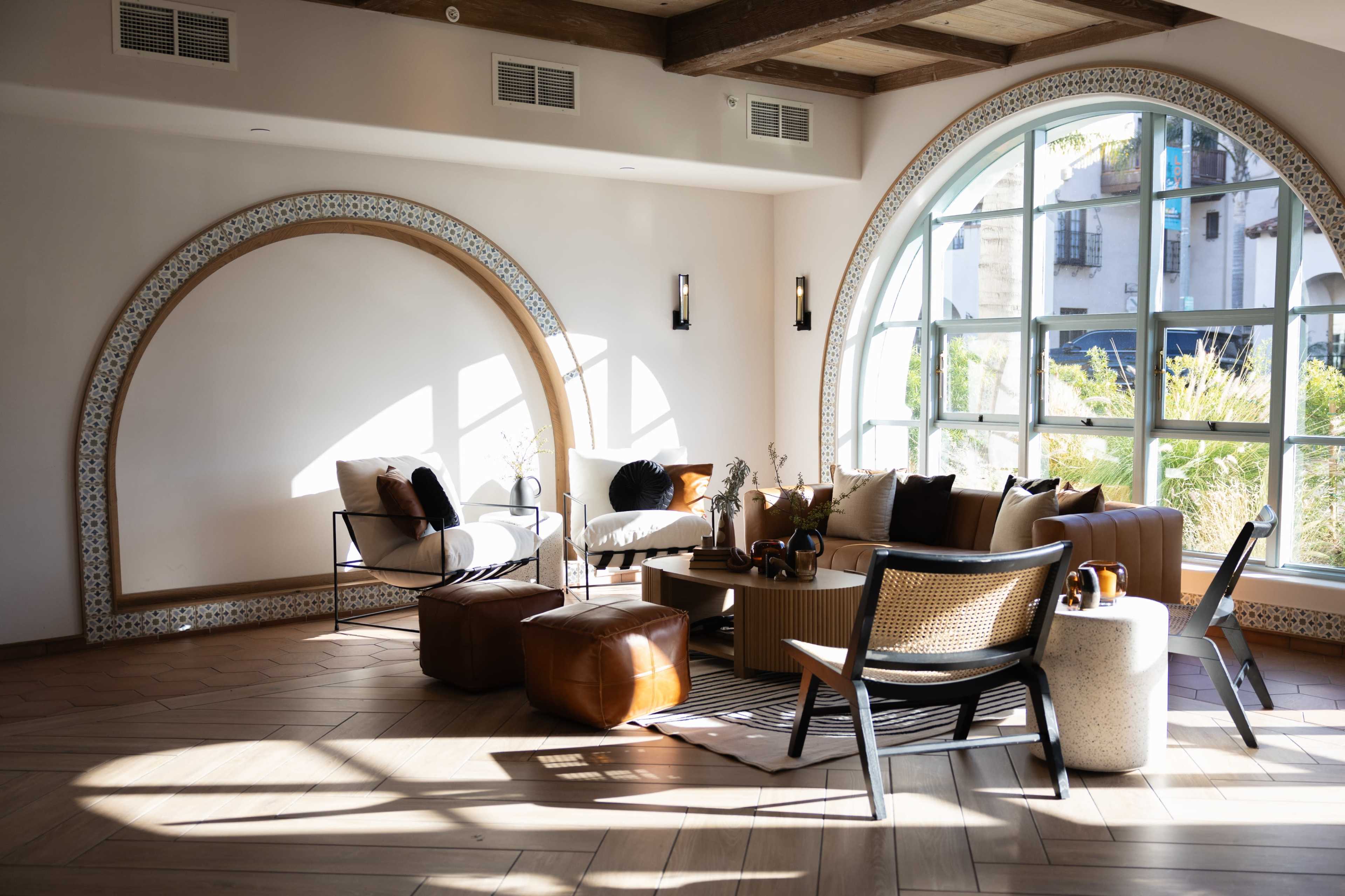 A well-lit modern lounge area featuring a mix of seating options, including armchairs and a sectional sofa, next to large arched windows.