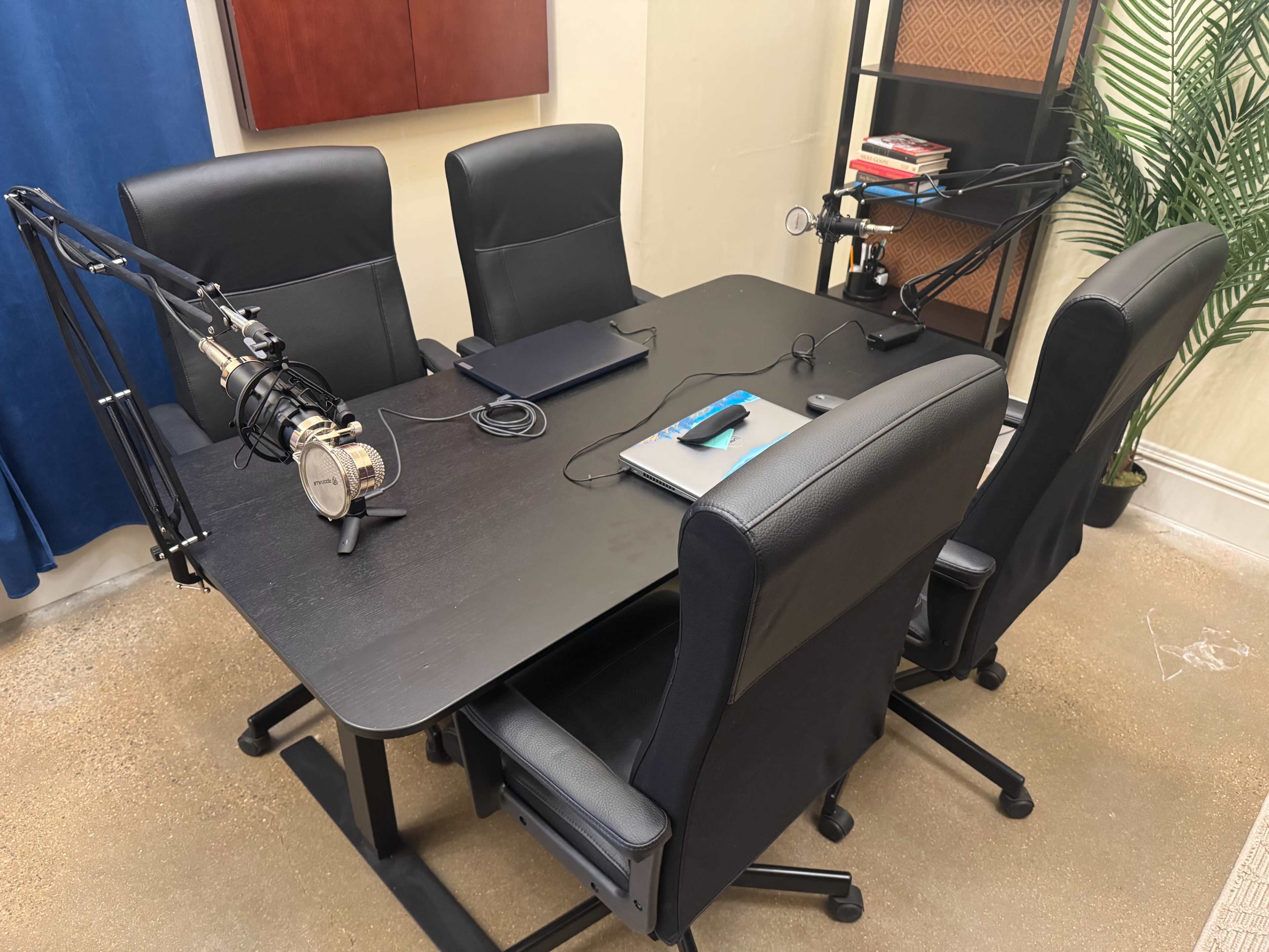 The image shows a conference table surrounded by four black office chairs, with two microphones mounted on stands and a laptop on the table.