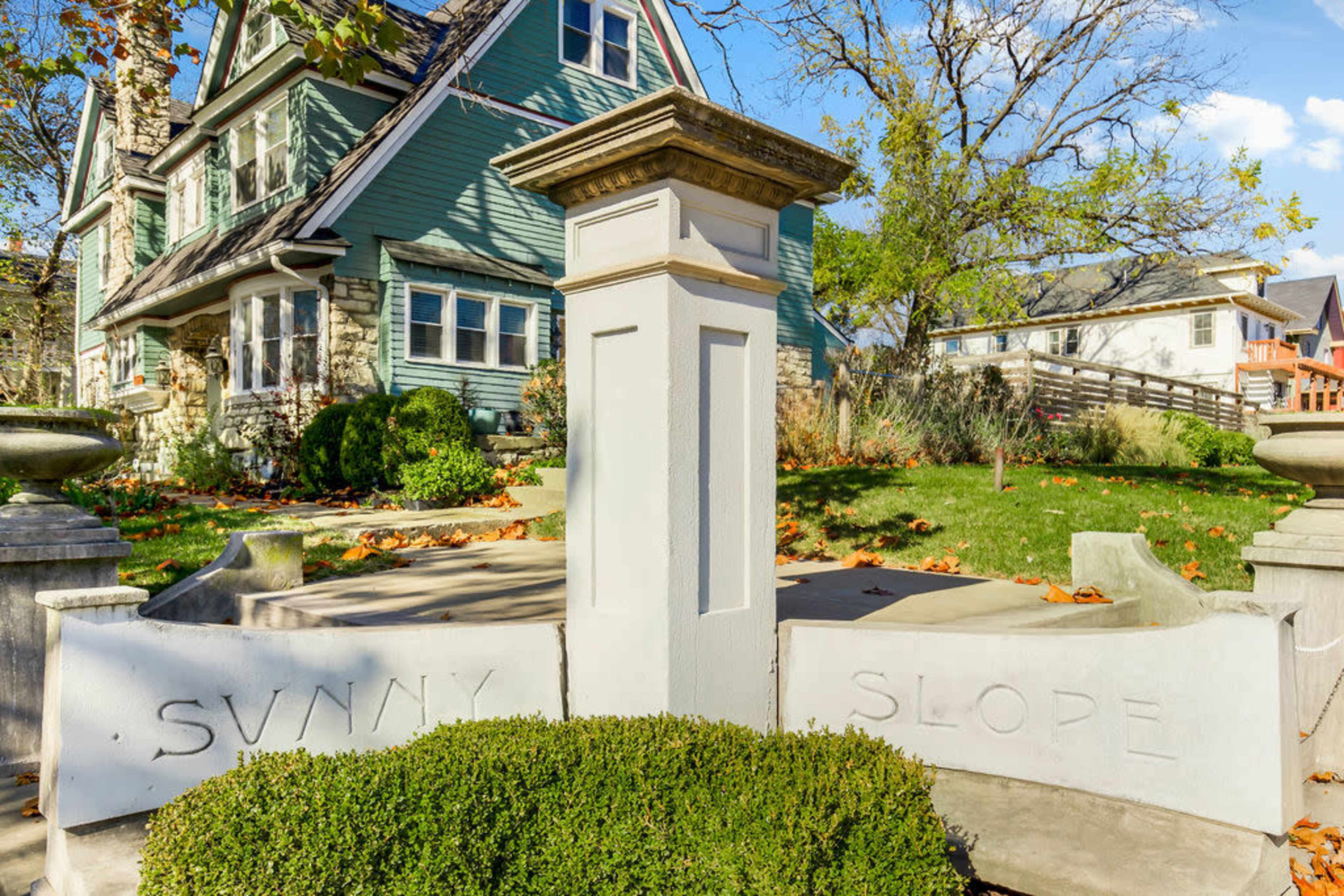 A well-maintained house with green siding and stone accents is visible behind a decorative entrance featuring the engraved words "Sunny Slope."