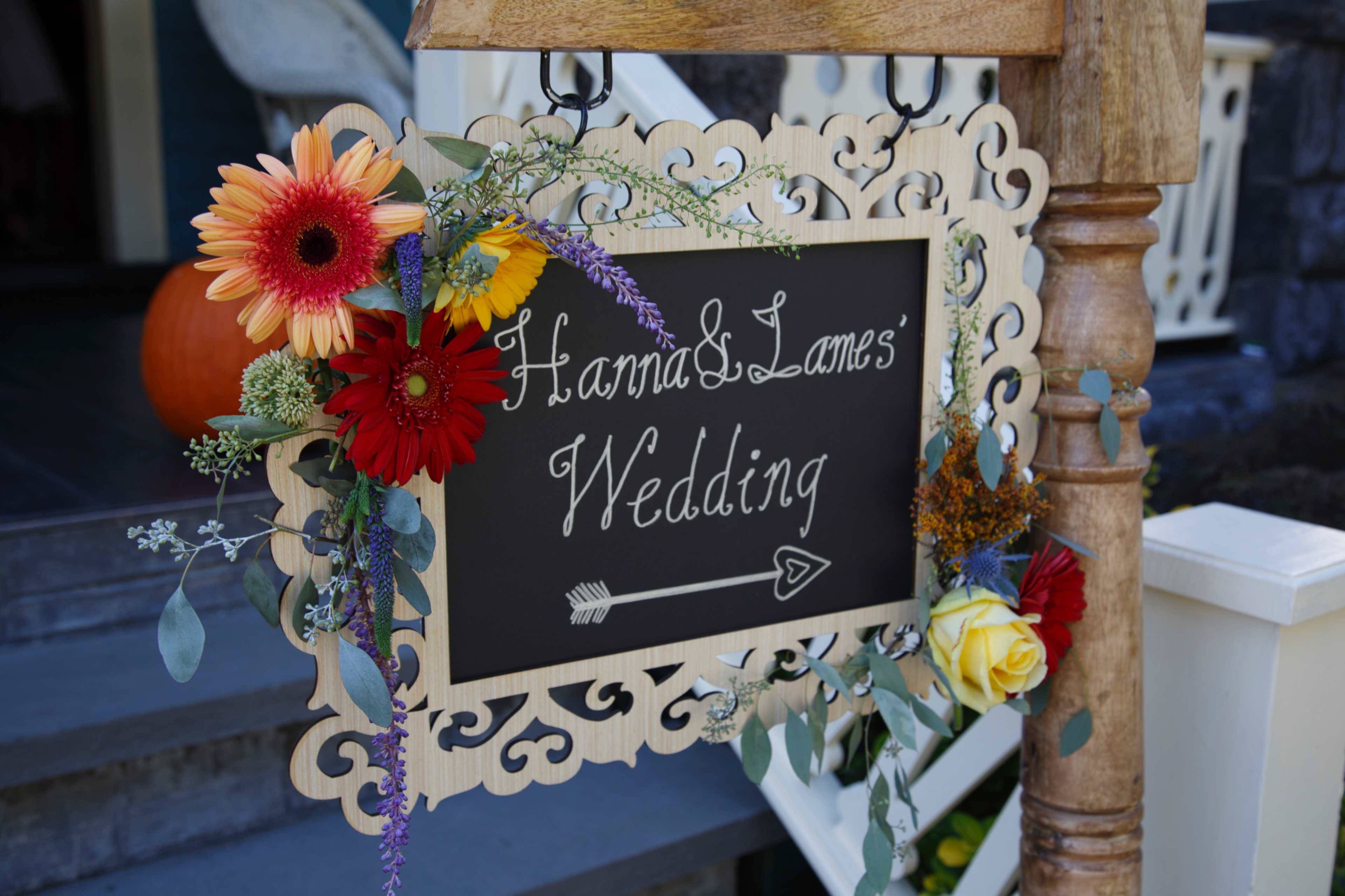 A decorative wooden sign adorned with flowers announces "Hanna & Lane's Wedding."