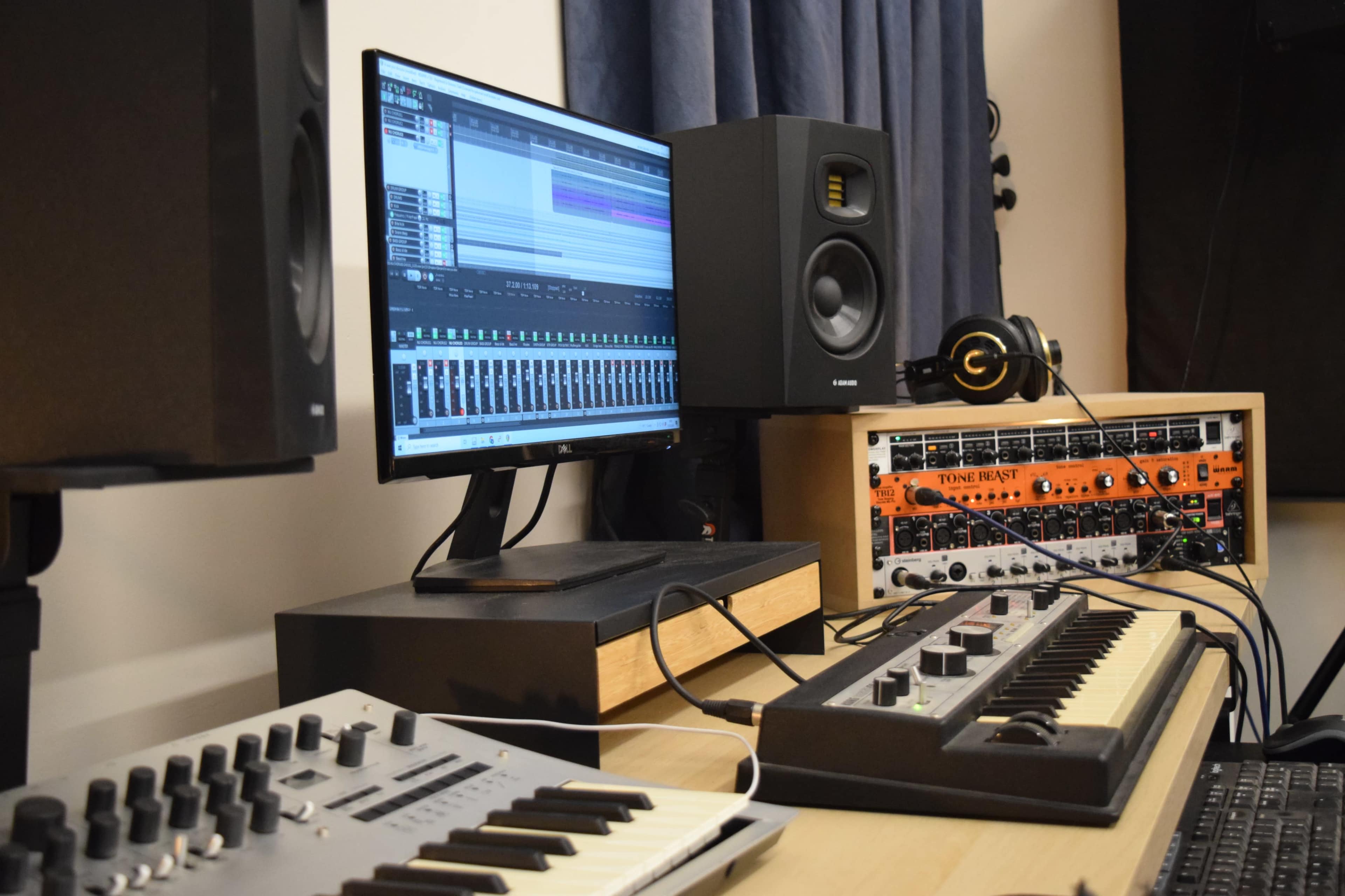 A music production setup featuring a computer monitor displaying audio software, studio monitors, a synthesizer, and a modular synthesizer.