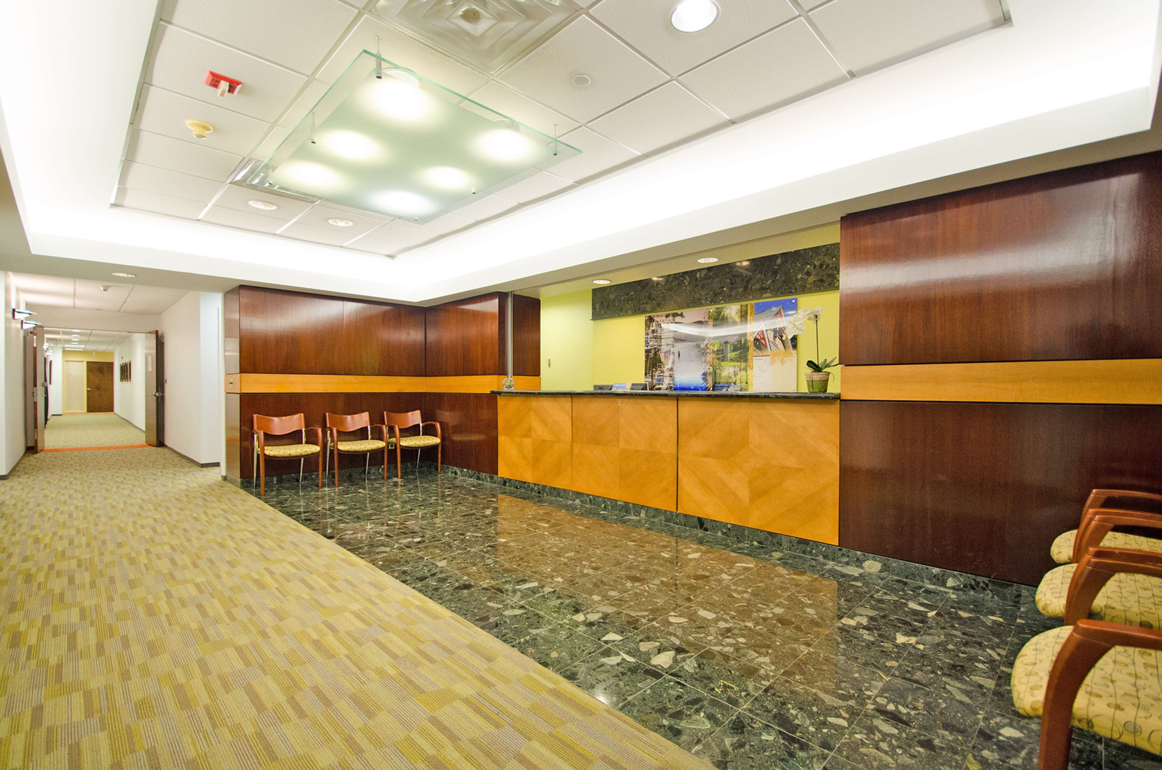 A modern reception area with a wooden front desk and seating along the walls, featuring a patterned carpet and glossy dark tile flooring.