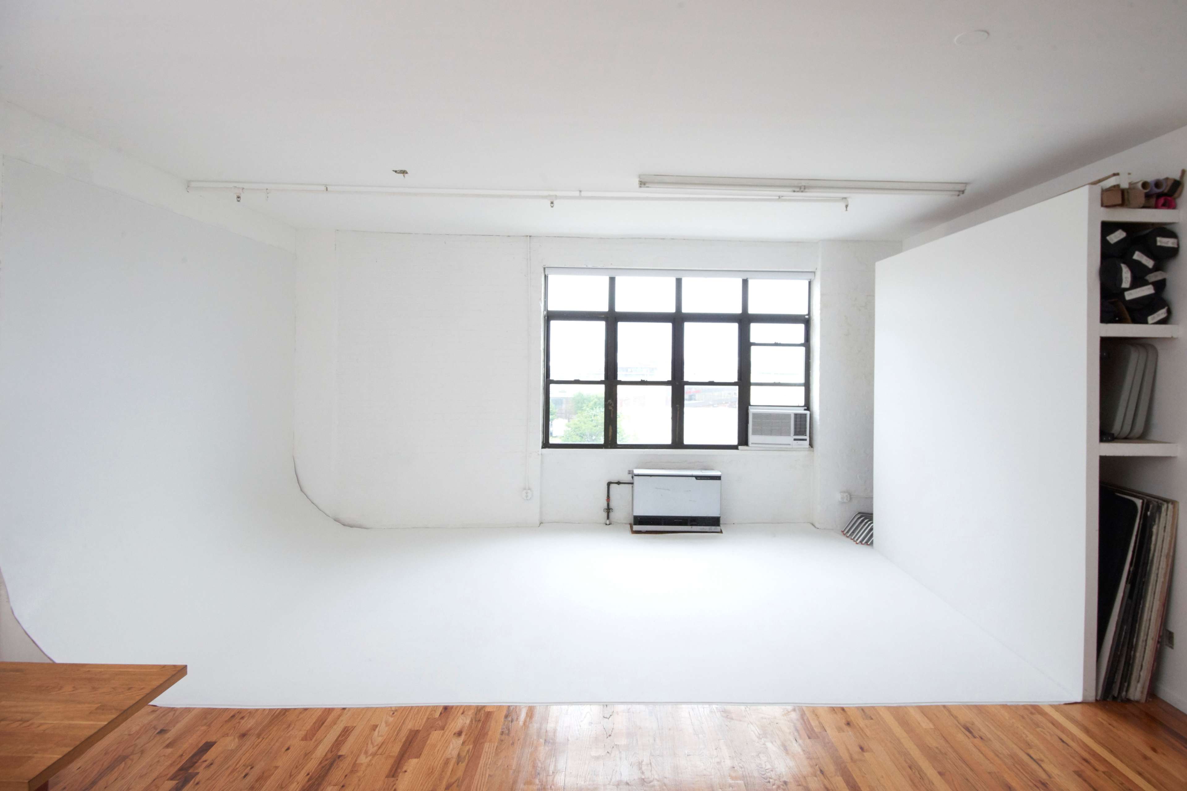 The image depicts a bright, empty photo studio with a seamless white backdrop and wooden flooring.