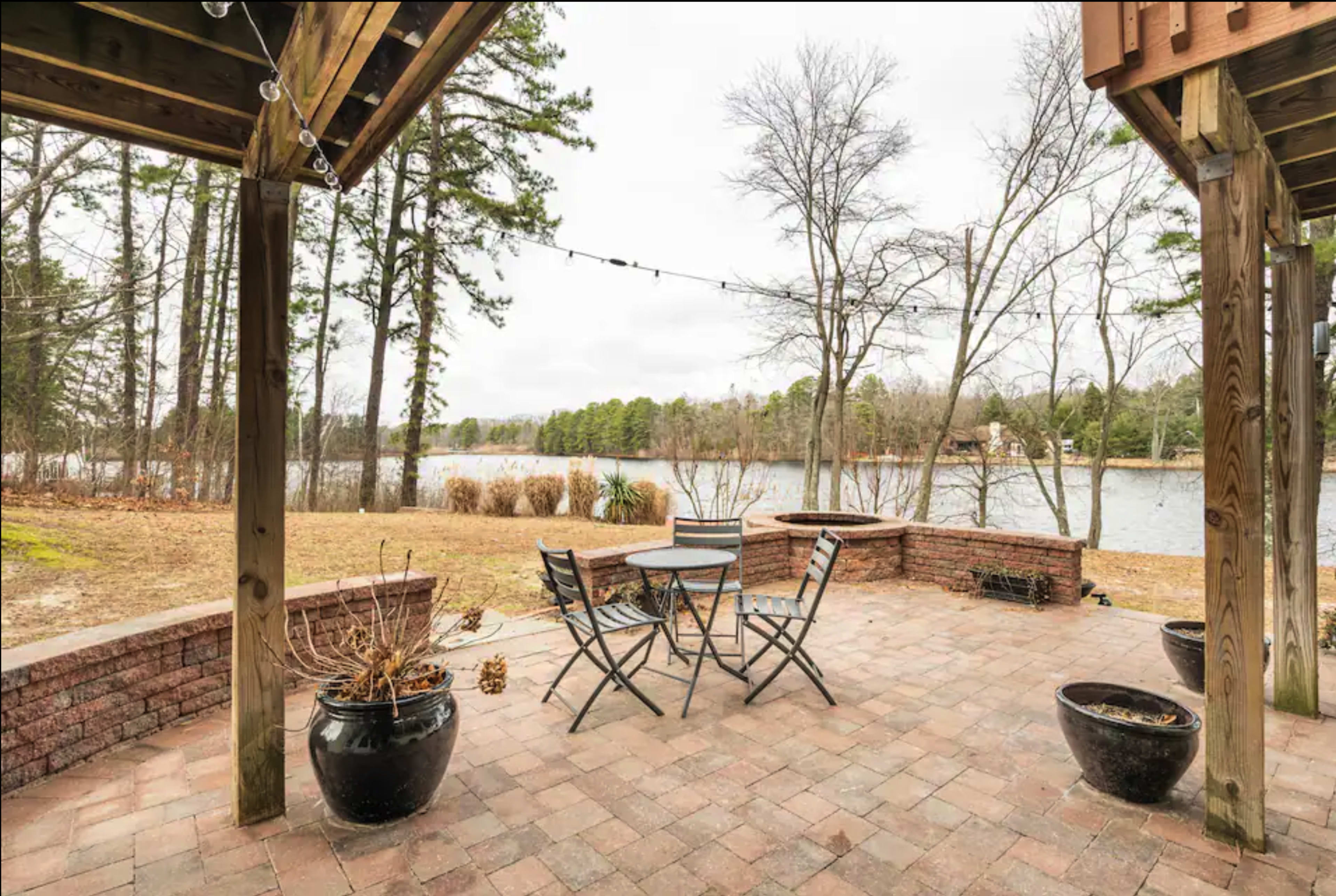 A patio with a table and chairs overlooks a calm lake surrounded by trees.
