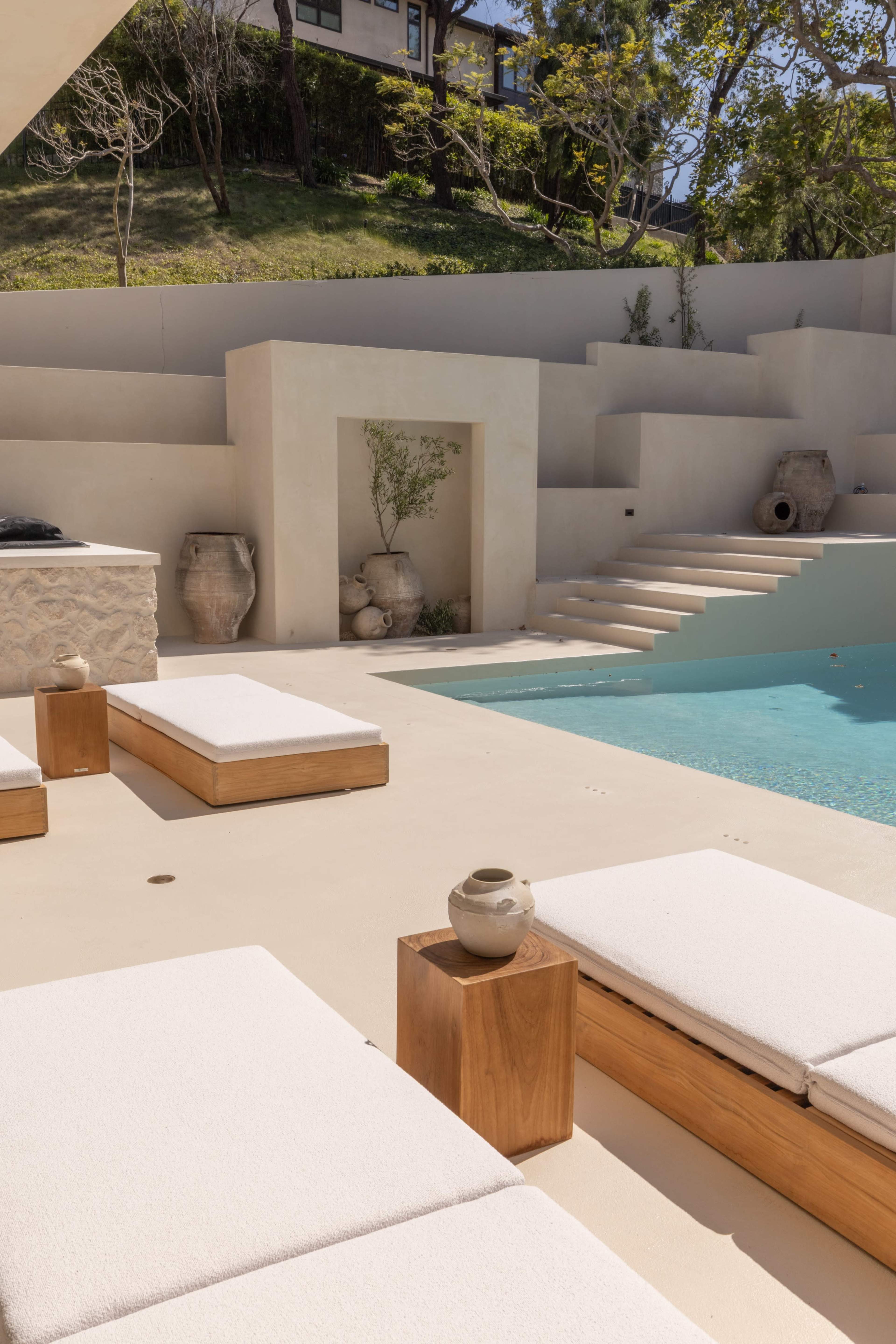 The image features a modern outdoor pool area with minimalist lounge chairs, wooden accents, and a landscaped background.