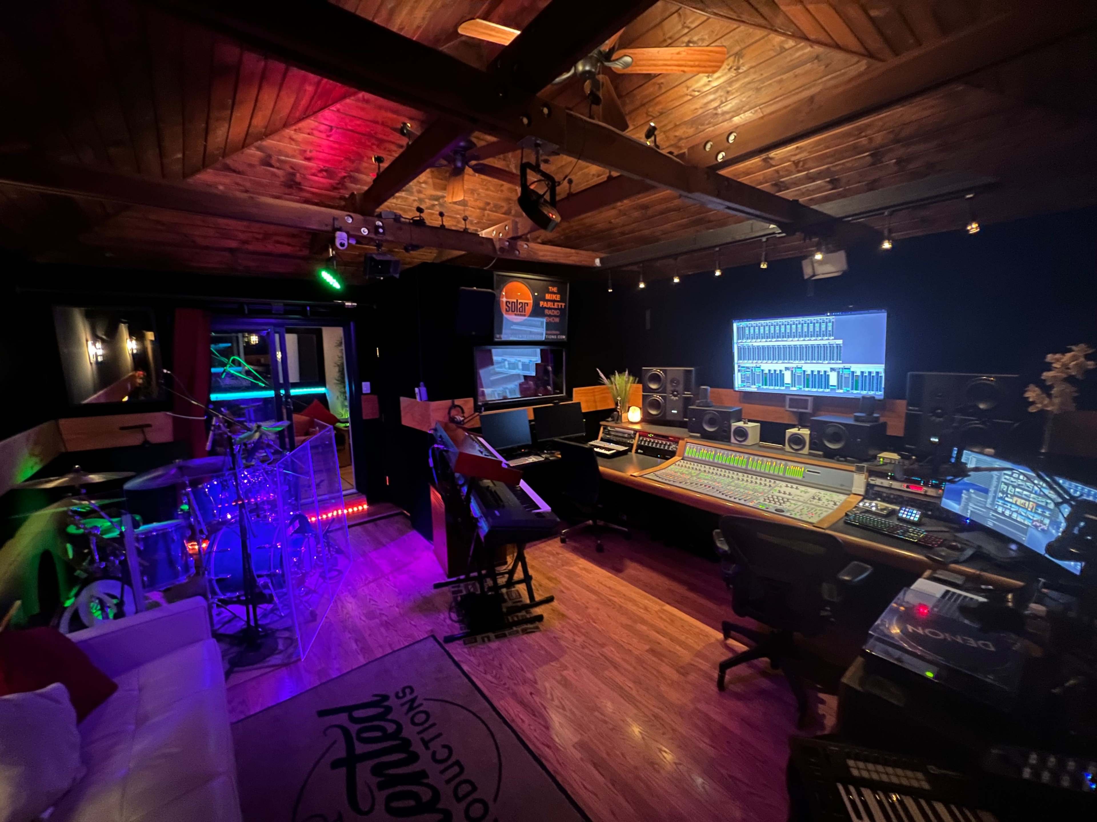 The image features a music studio with a mixing console, various instruments, and colorful lighting, all under a wooden ceiling.