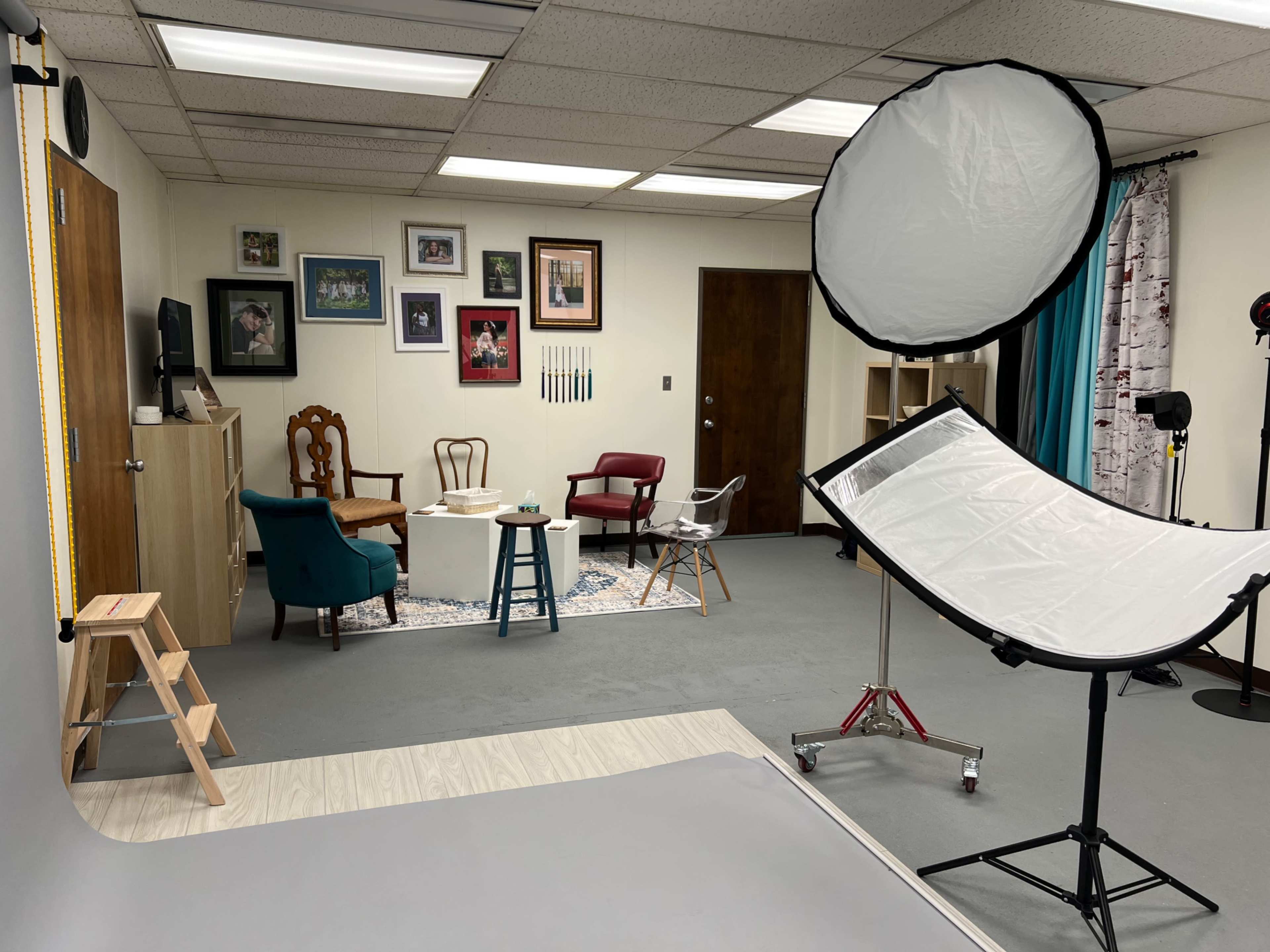 The image shows a photography studio equipped with a backdrop setup, various chairs, a table, and decorative wall frames.