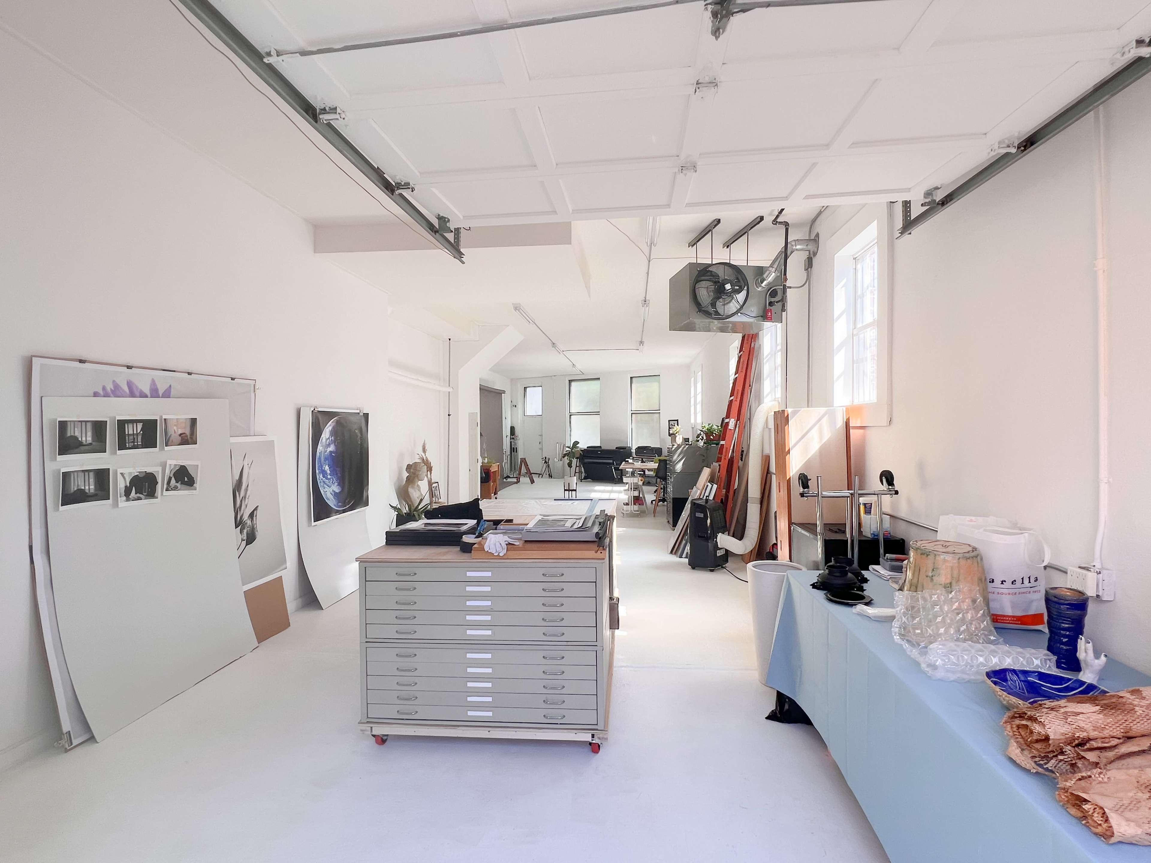 A spacious art studio with white walls, a mix of artworks displayed, and various tools and materials arranged throughout the room.
