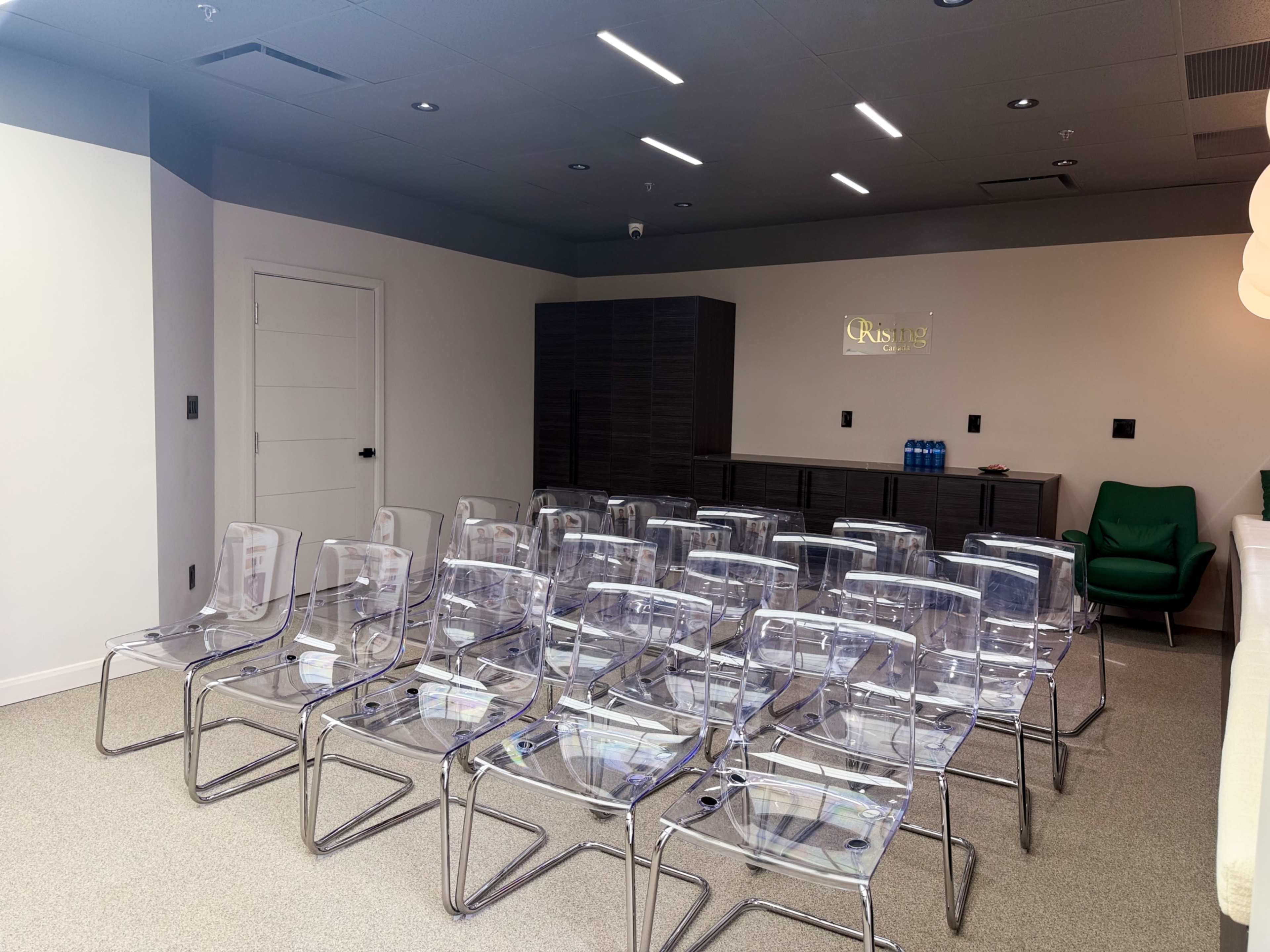 The image shows a meeting room featuring transparent chairs arranged in rows, with a dark cabinet and a green chair in the background.