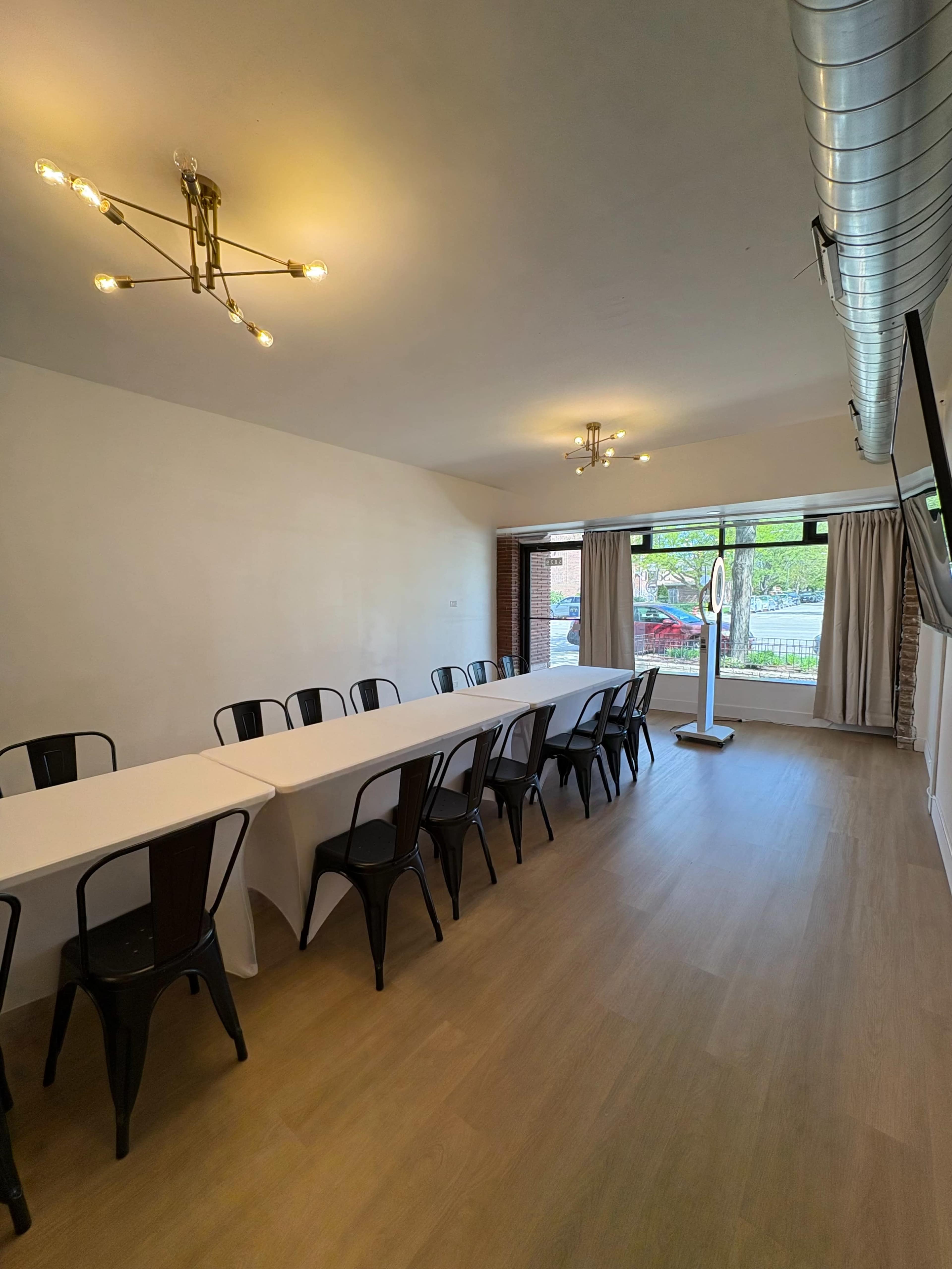 The image shows a well-lit dining area with a long table set for a gathering, surrounded by modern decor and large windows.