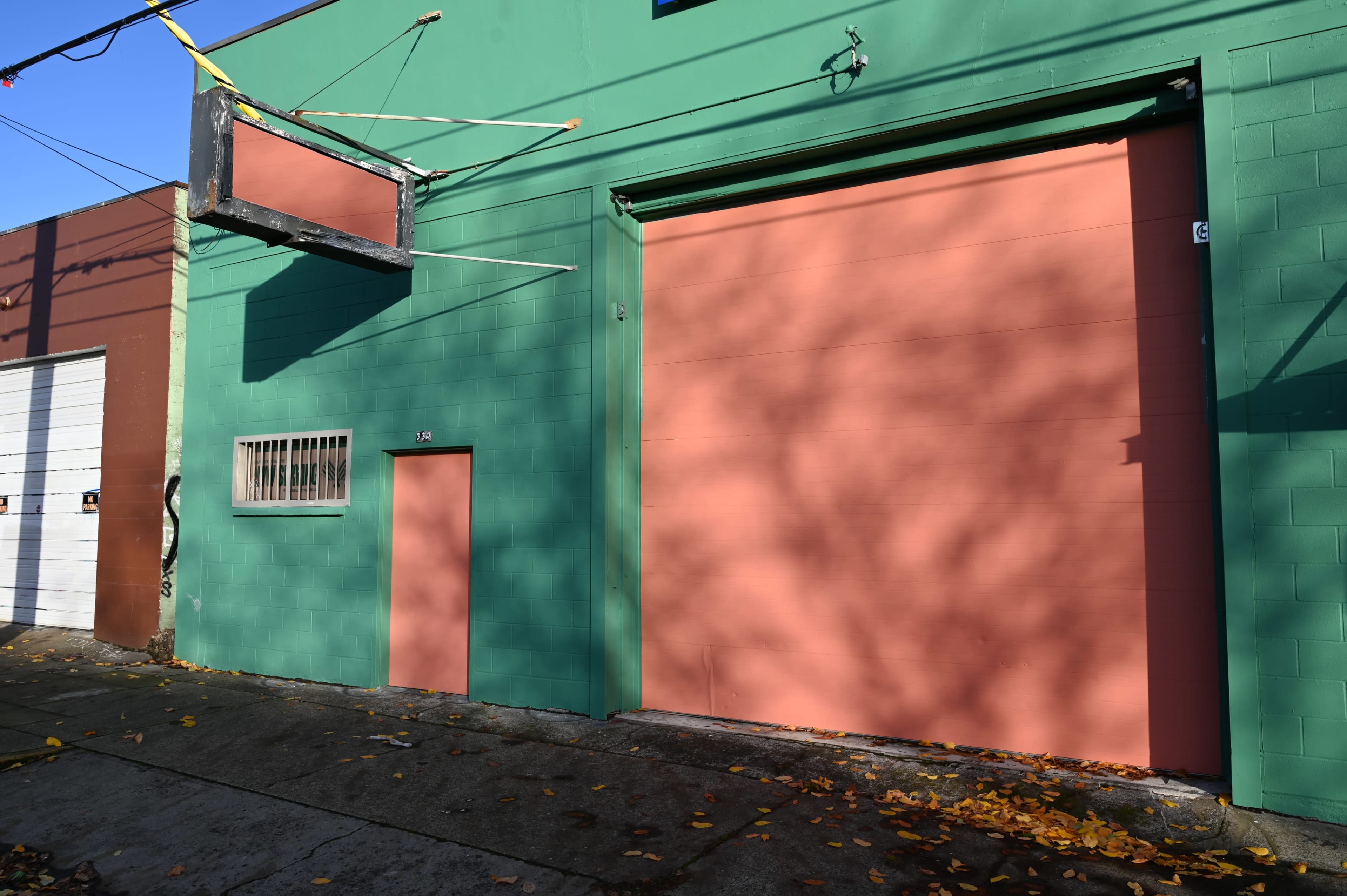 The image shows a green building with a large pink garage door, a small door, and a sign hanging above.
