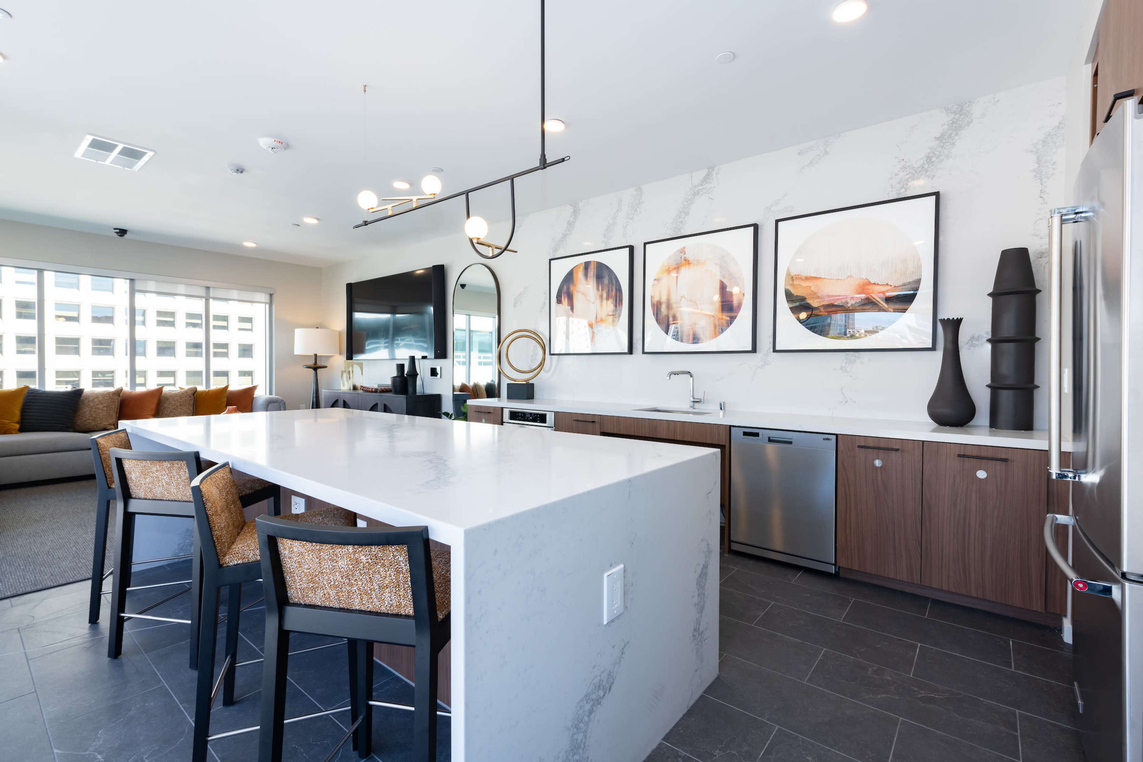 A modern kitchen with a large white island, dark cabinetry, and three bar stools, featuring decorative artwork on the wall.