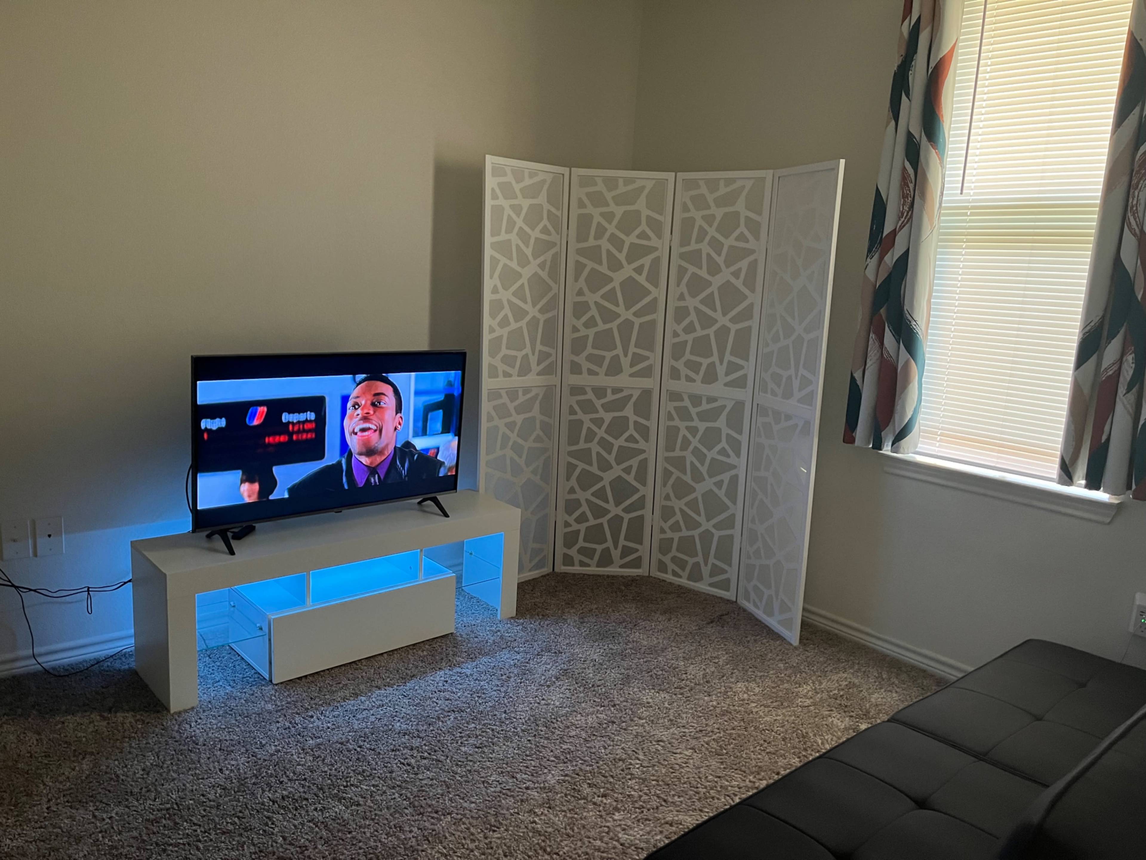 A modern living room features a television on a white stand with blue lighting, positioned next to a decorative partition and a black sofa.