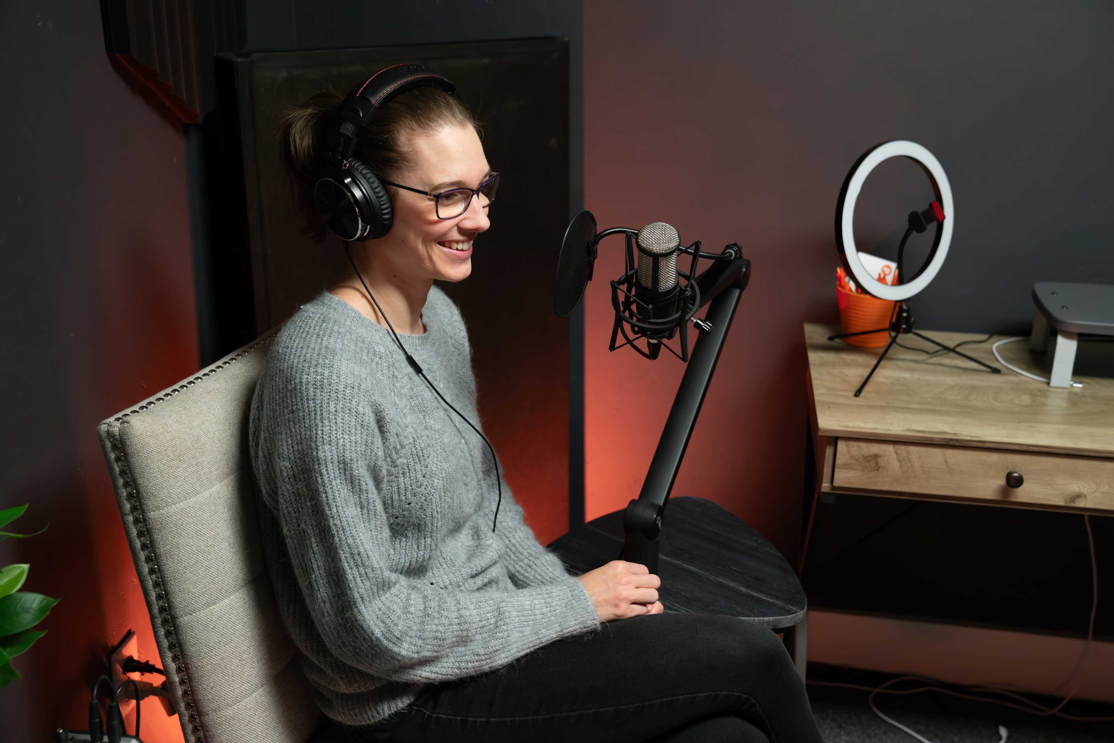 A woman wearing headphones sits in front of a microphone in a recording studio.