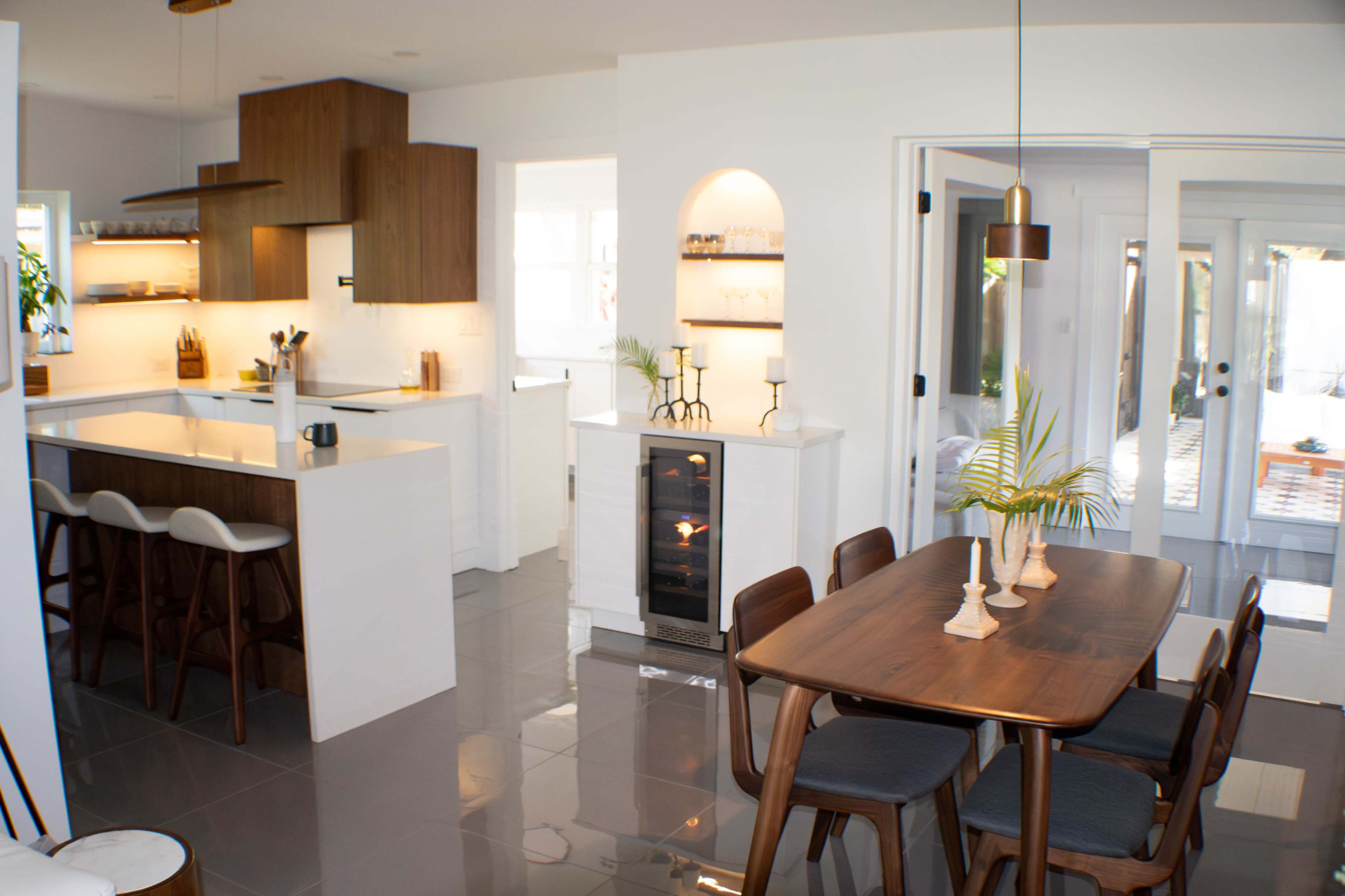 A modern kitchen and dining area featuring a sleek island with bar stools, a wooden dining table, and a wine cooler.