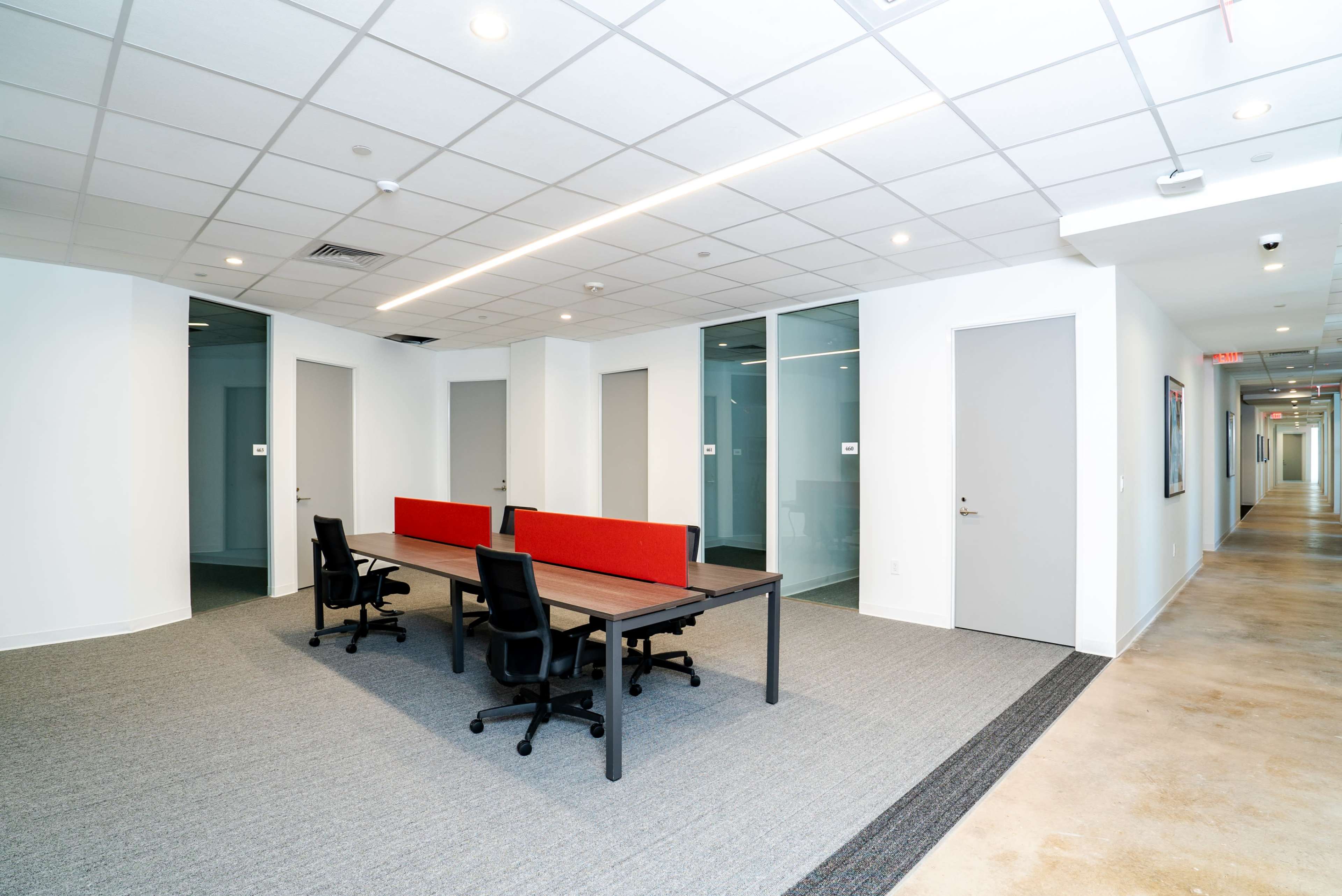 A modern office space features a rectangular table with chairs and a carpeted floor, flanked by a hallway with closed doors.