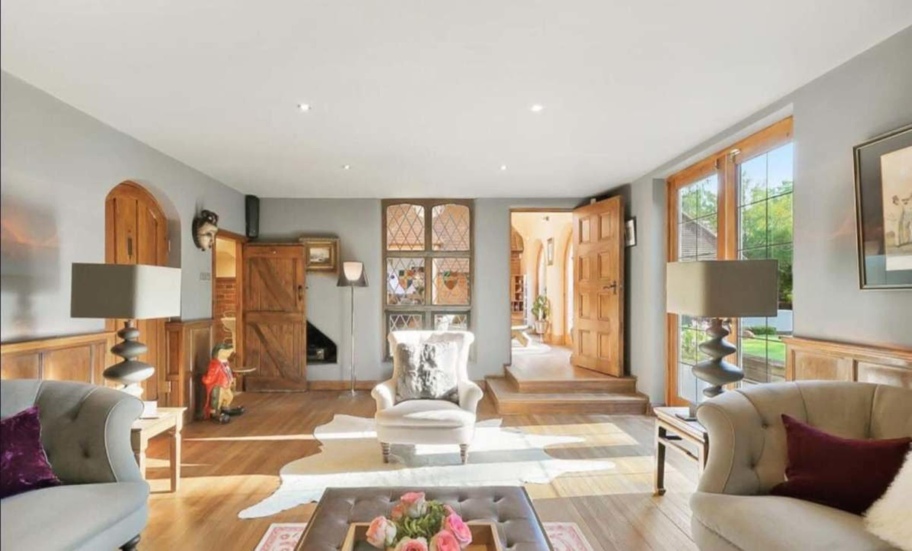 The image shows a bright living room with two sofas, a coffee table in the center, and large windows allowing natural light to enter.