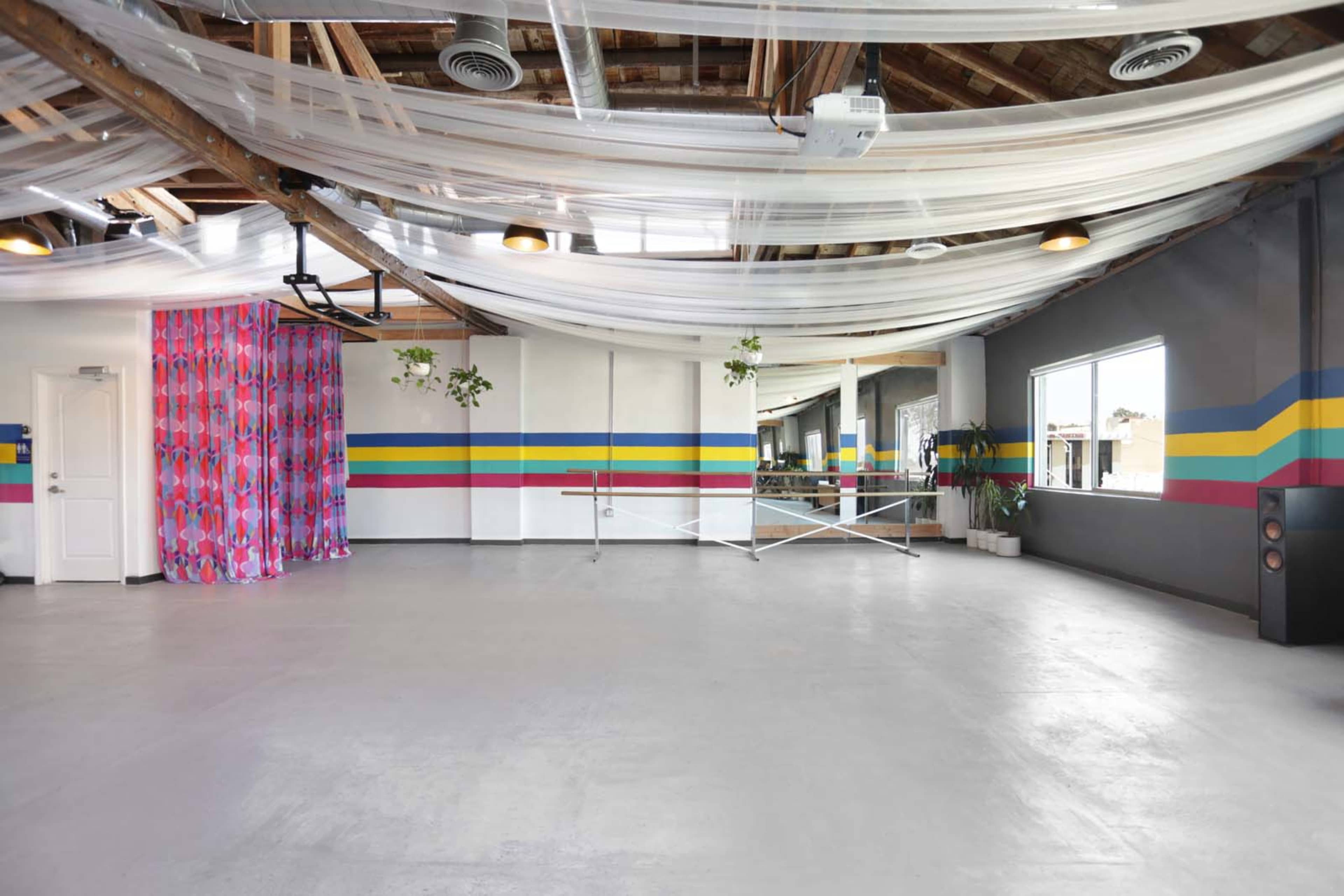 The image shows a large, open room with a polished concrete floor, colorful stripes on the walls, and draped fabric overhead.
