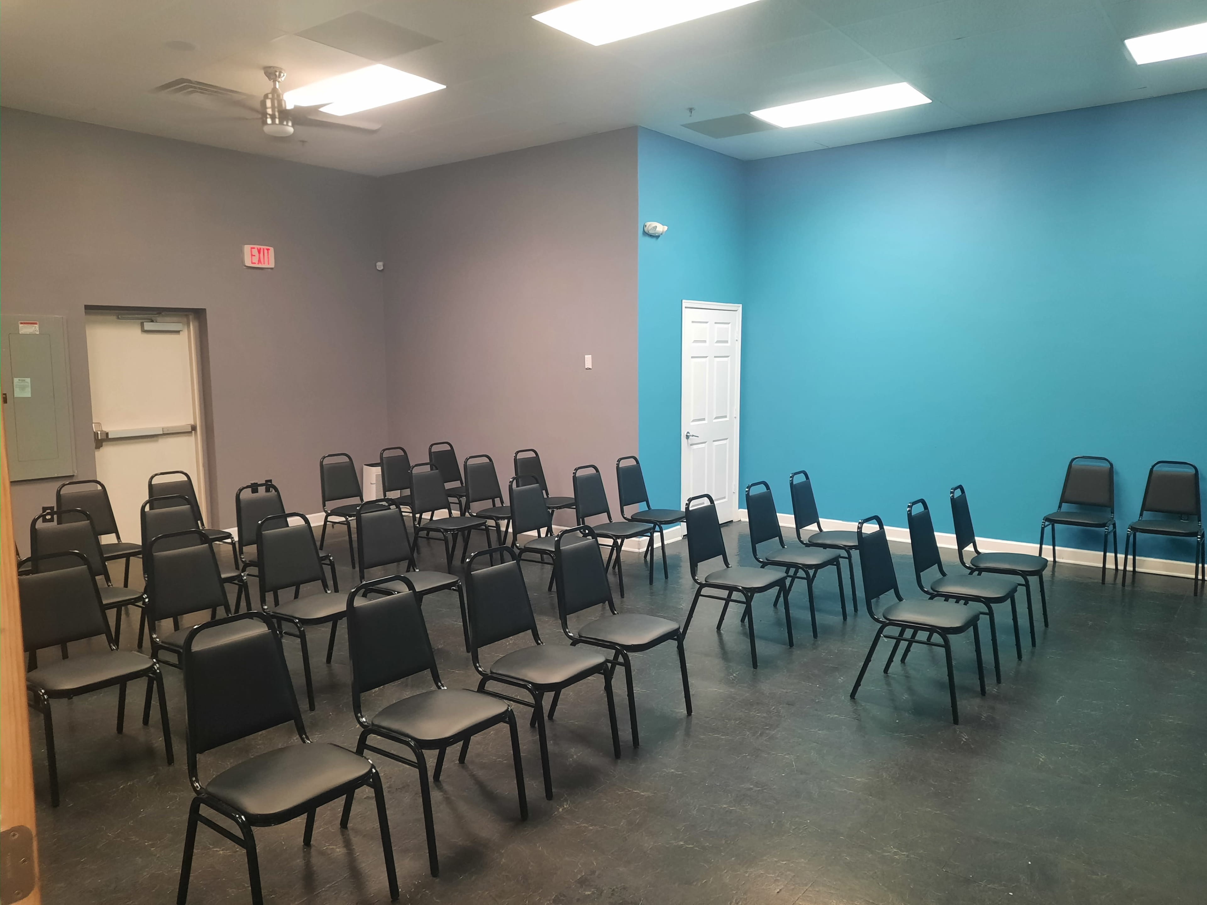 A room with an arrangement of black chairs facing a blue wall, with additional chairs against the side wall.