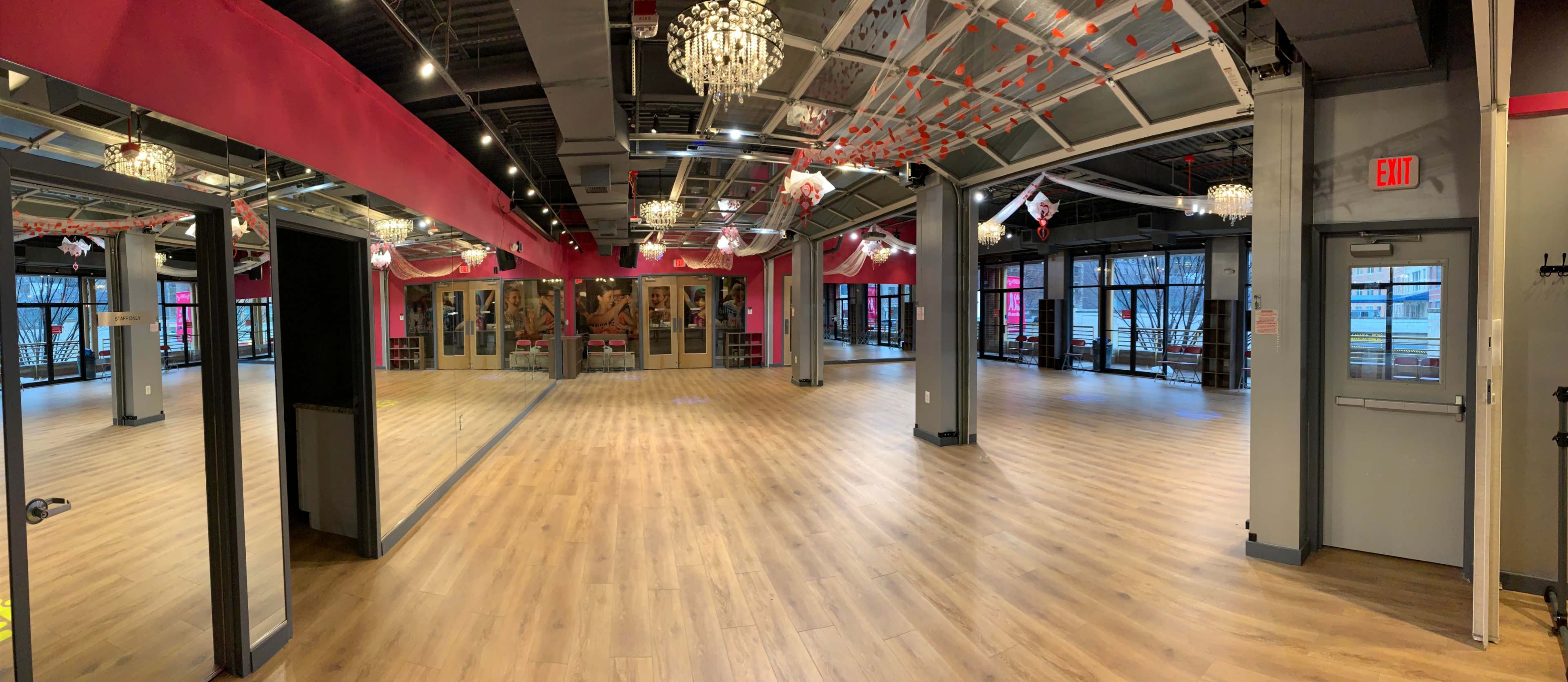 A spacious dance studio features wooden flooring, large mirrors along one wall, and multiple windows providing natural light.