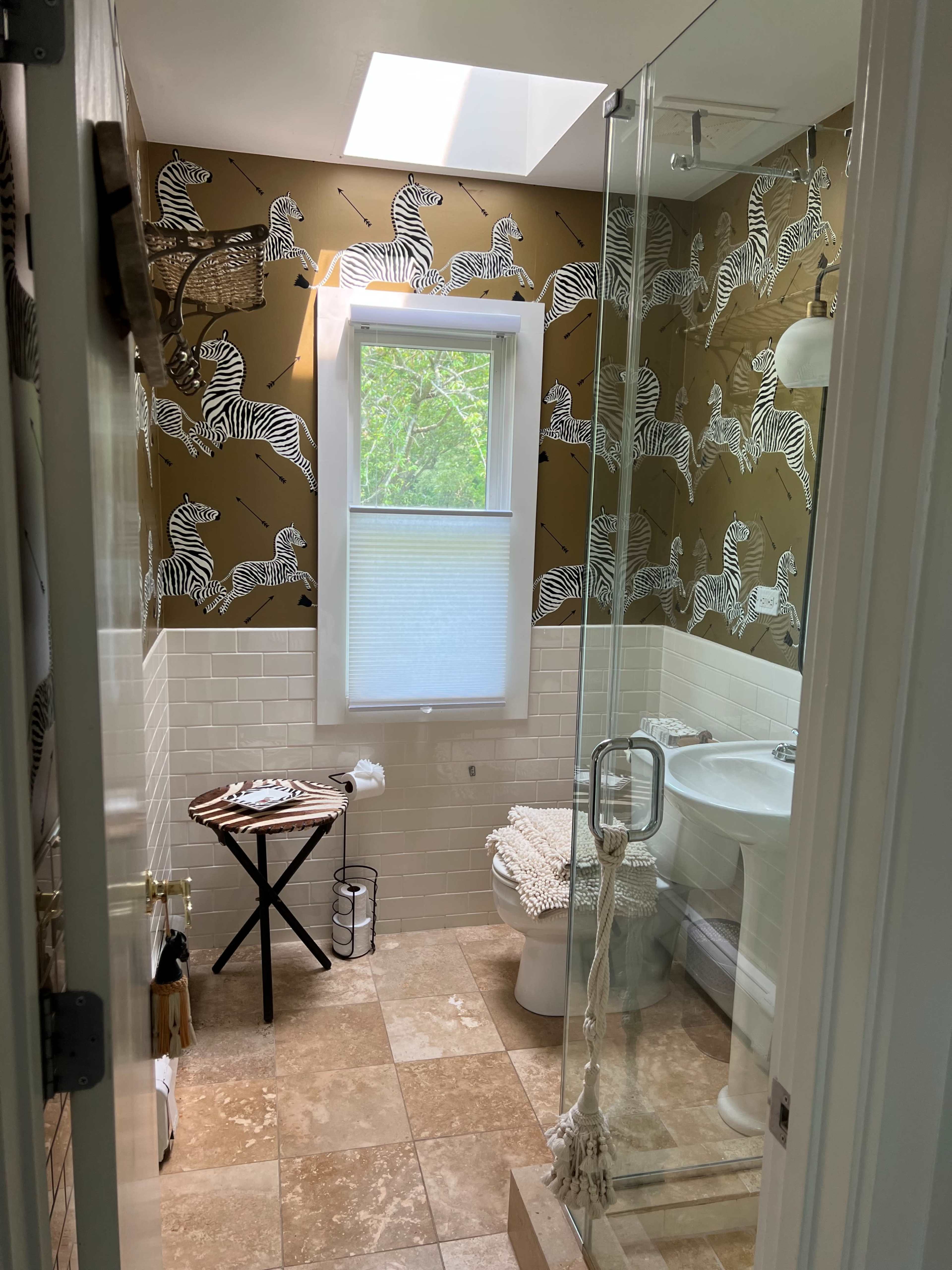 A bathroom featuring a zebra-patterned wallpaper, a shower with glass doors, and a white porcelain toilet and sink.