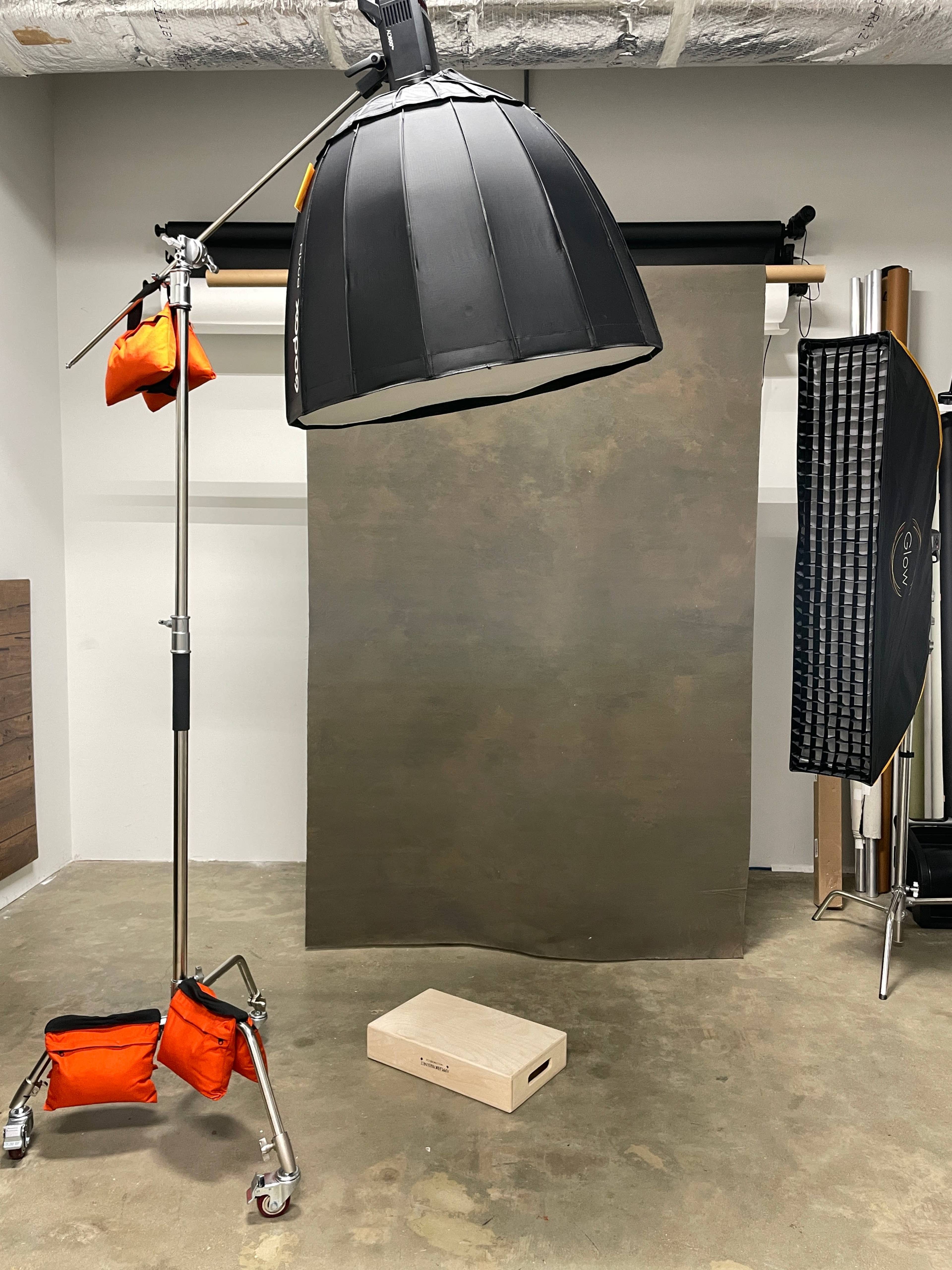 A photography studio with a large softbox light, a backdrop made of fabric, and a wooden box on the floor.