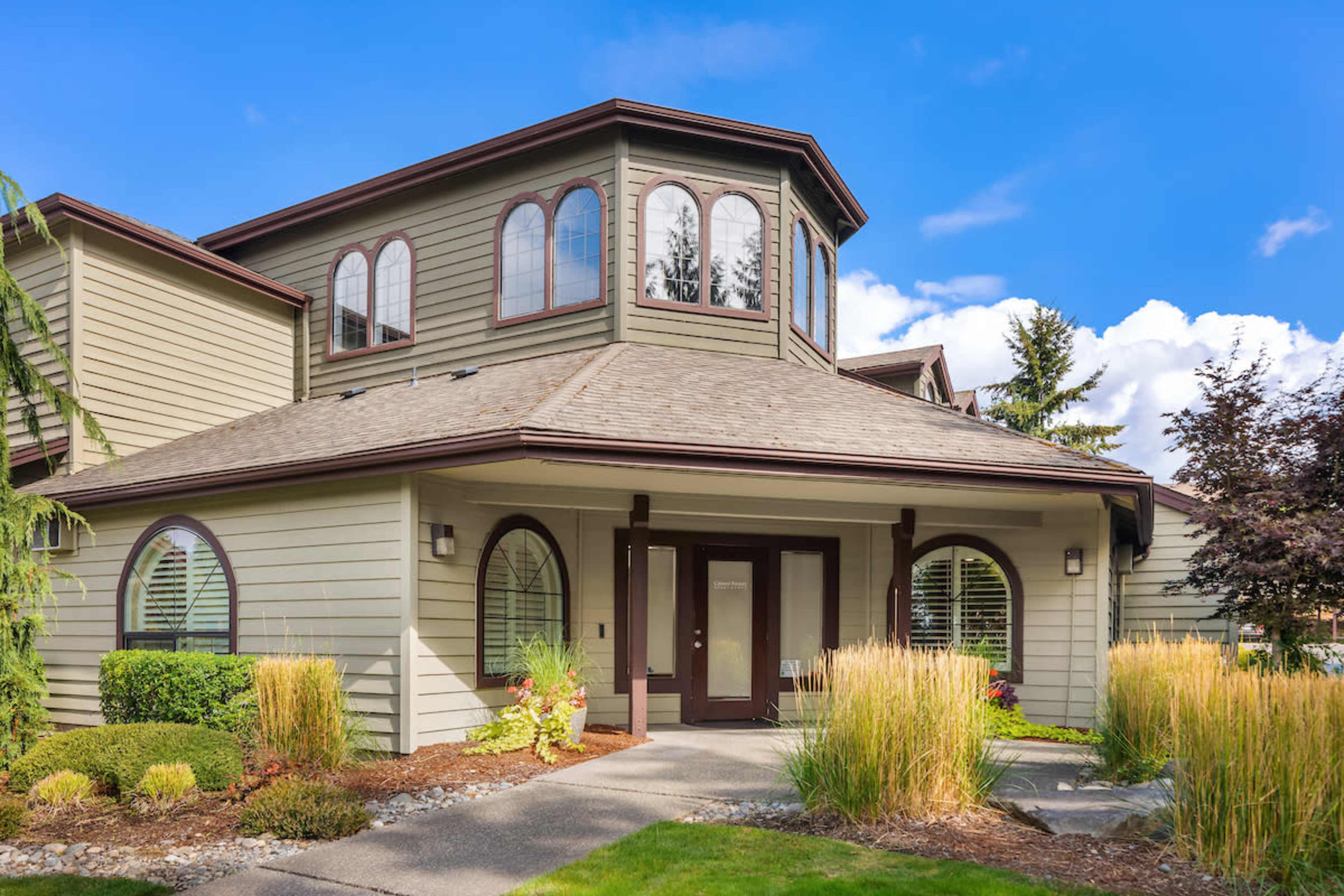 A two-story house with a circular turret, surrounded by landscaped greenery and a pathway leading to the entrance.