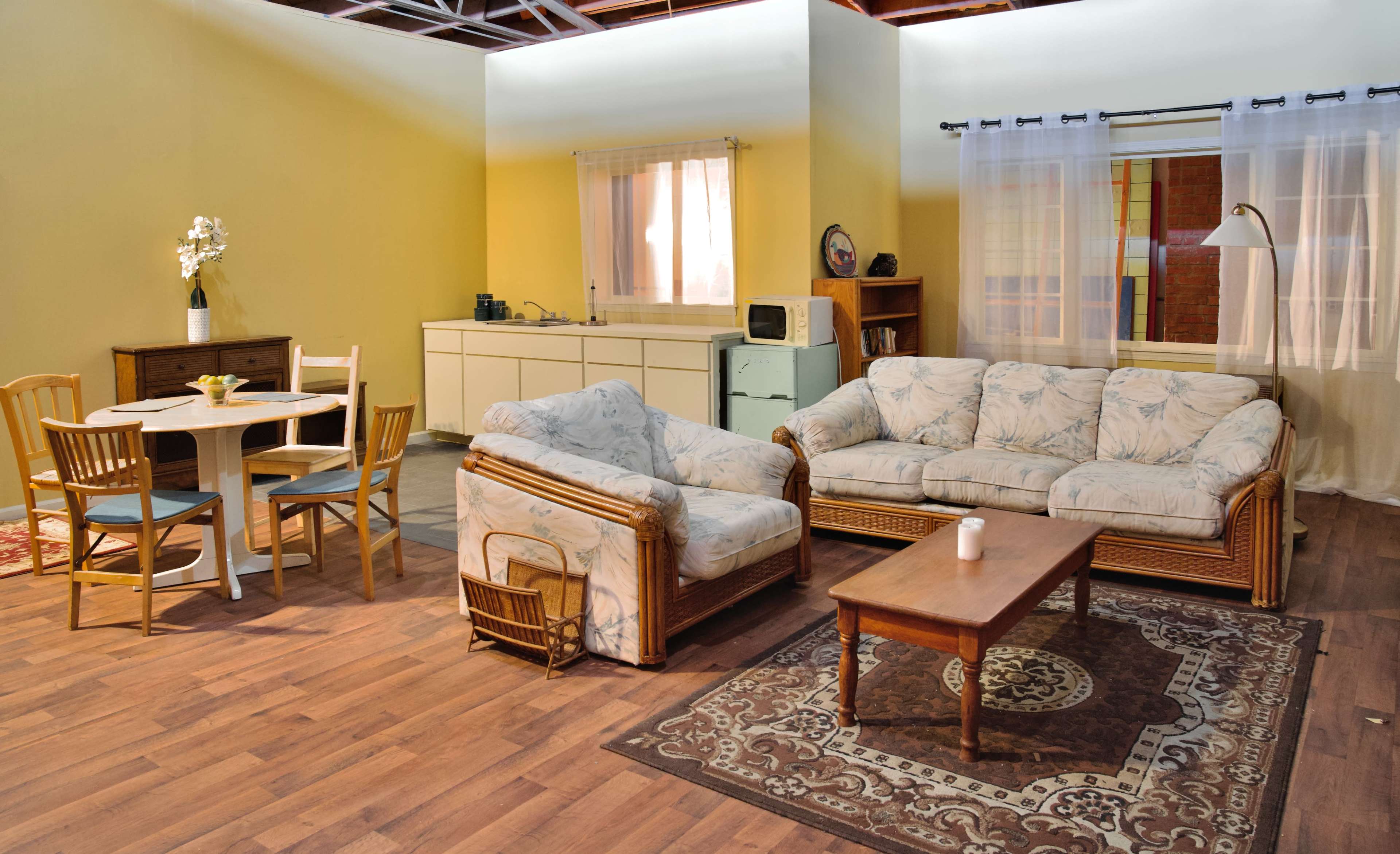 A living room with two light-colored sofas, a wooden coffee table, a dining table with chairs, and a kitchen area in the background.